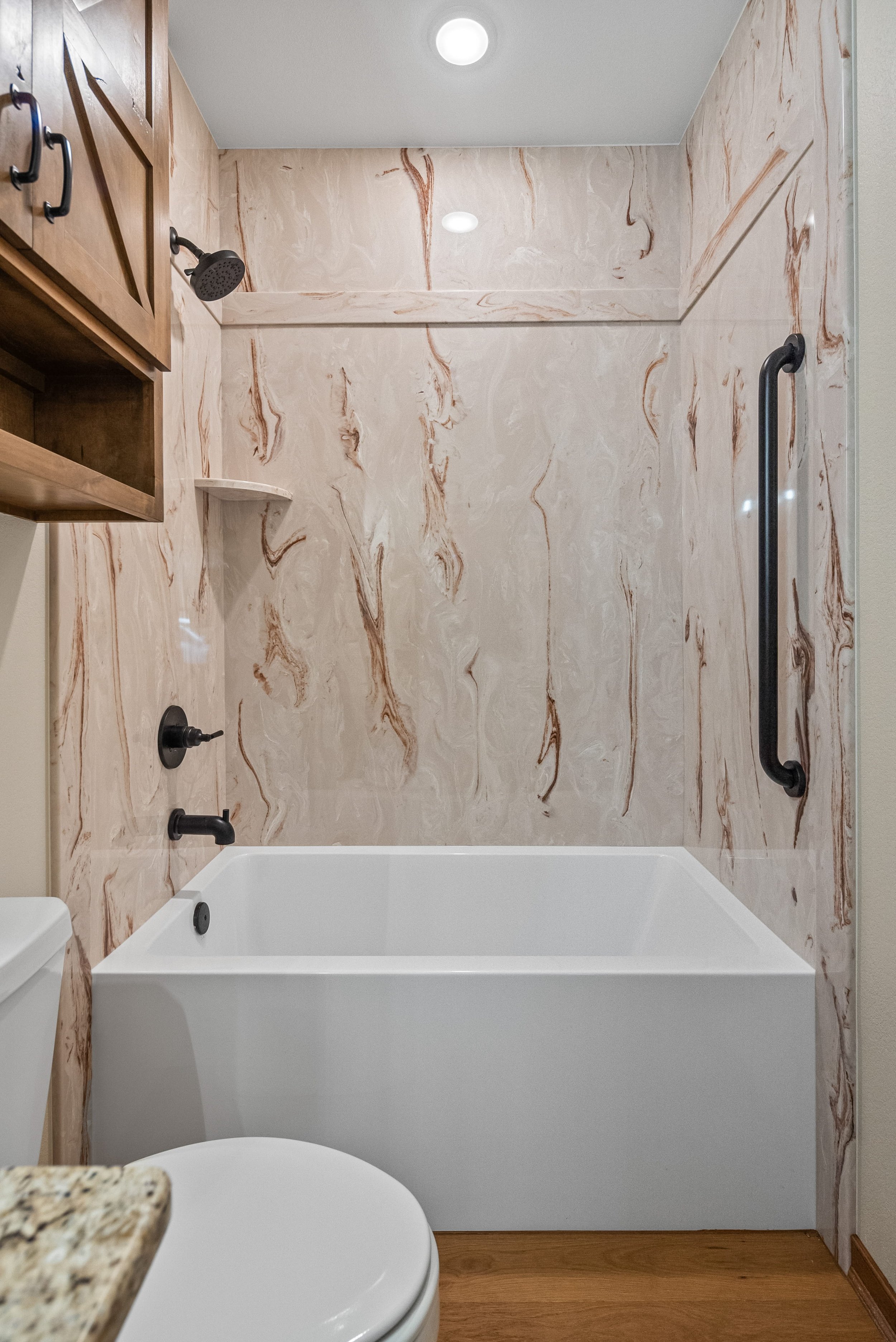 Bathroom with beige marble walls, a white bathtub, black fixtures, a wooden cabinet, and a granite countertop.