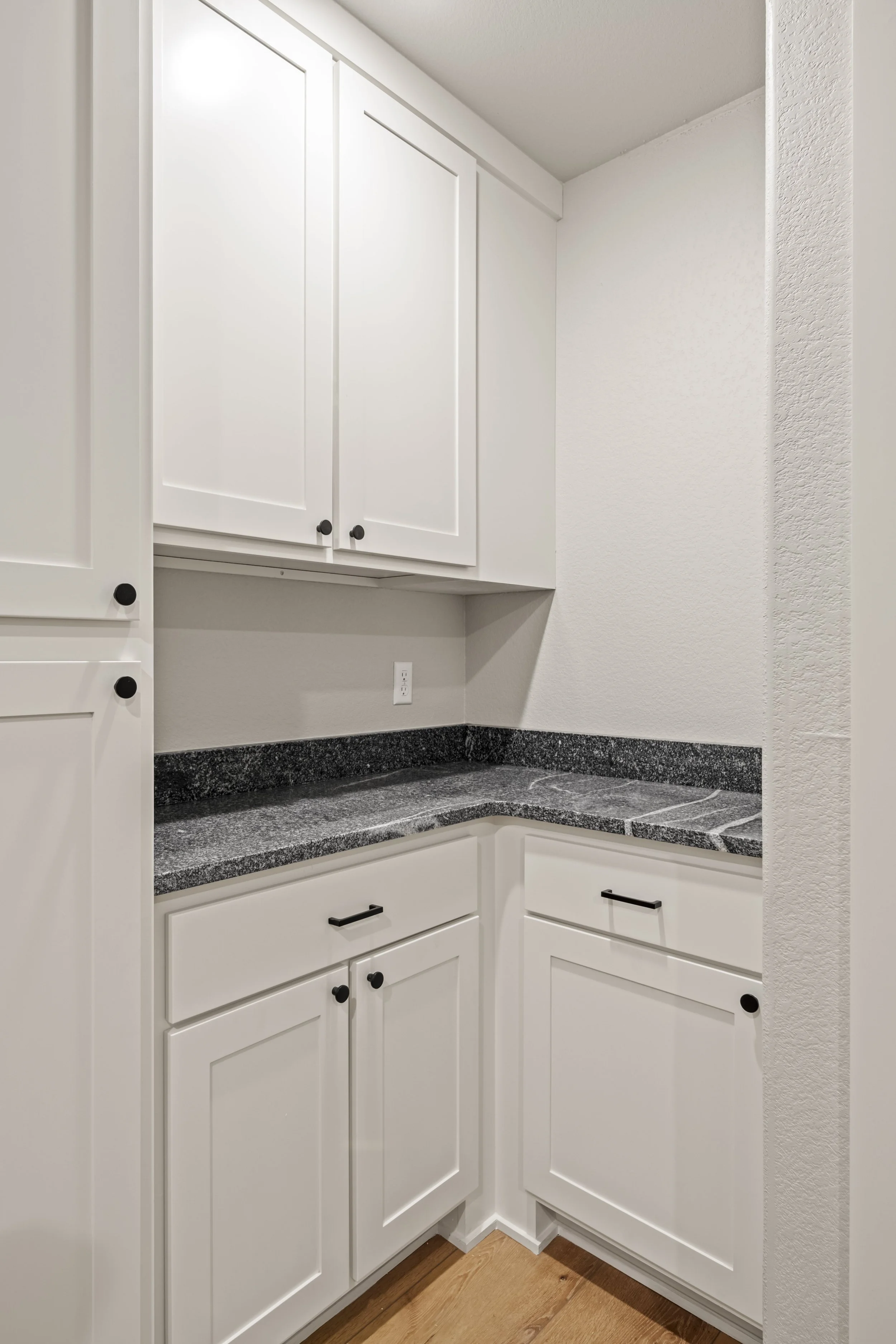 White kitchen cabinets with black hardware and a granite countertop in a corner.