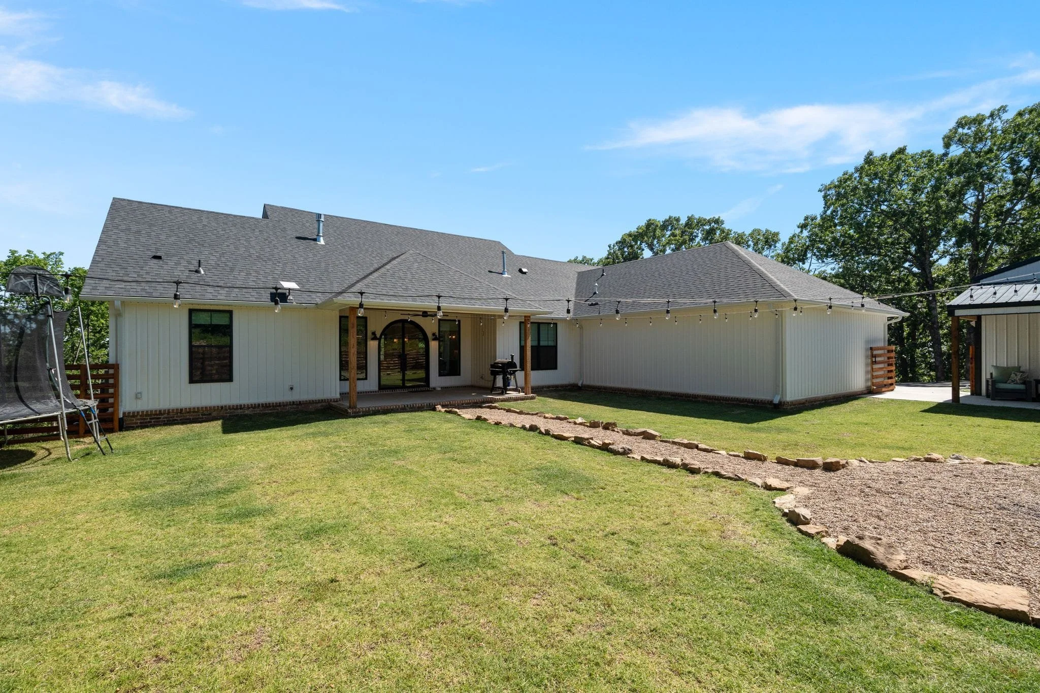 Angled backyard view of farmhouse with covered patio, string lights, and lawn