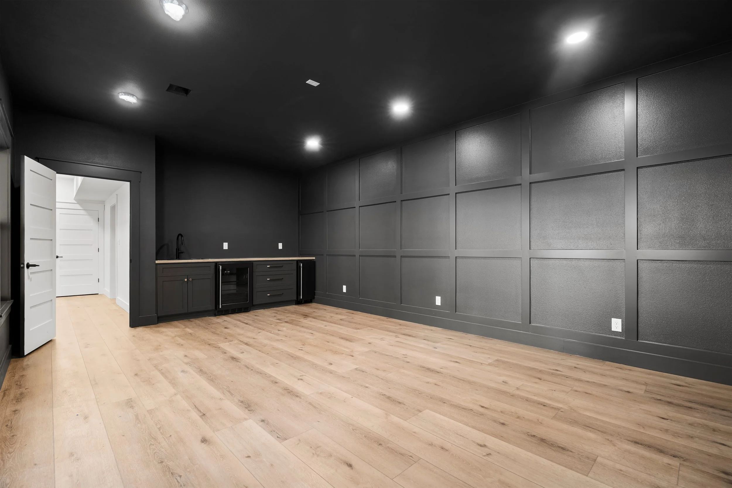 Empty room with black walls, wooden floor, and a small kitchenette area.
