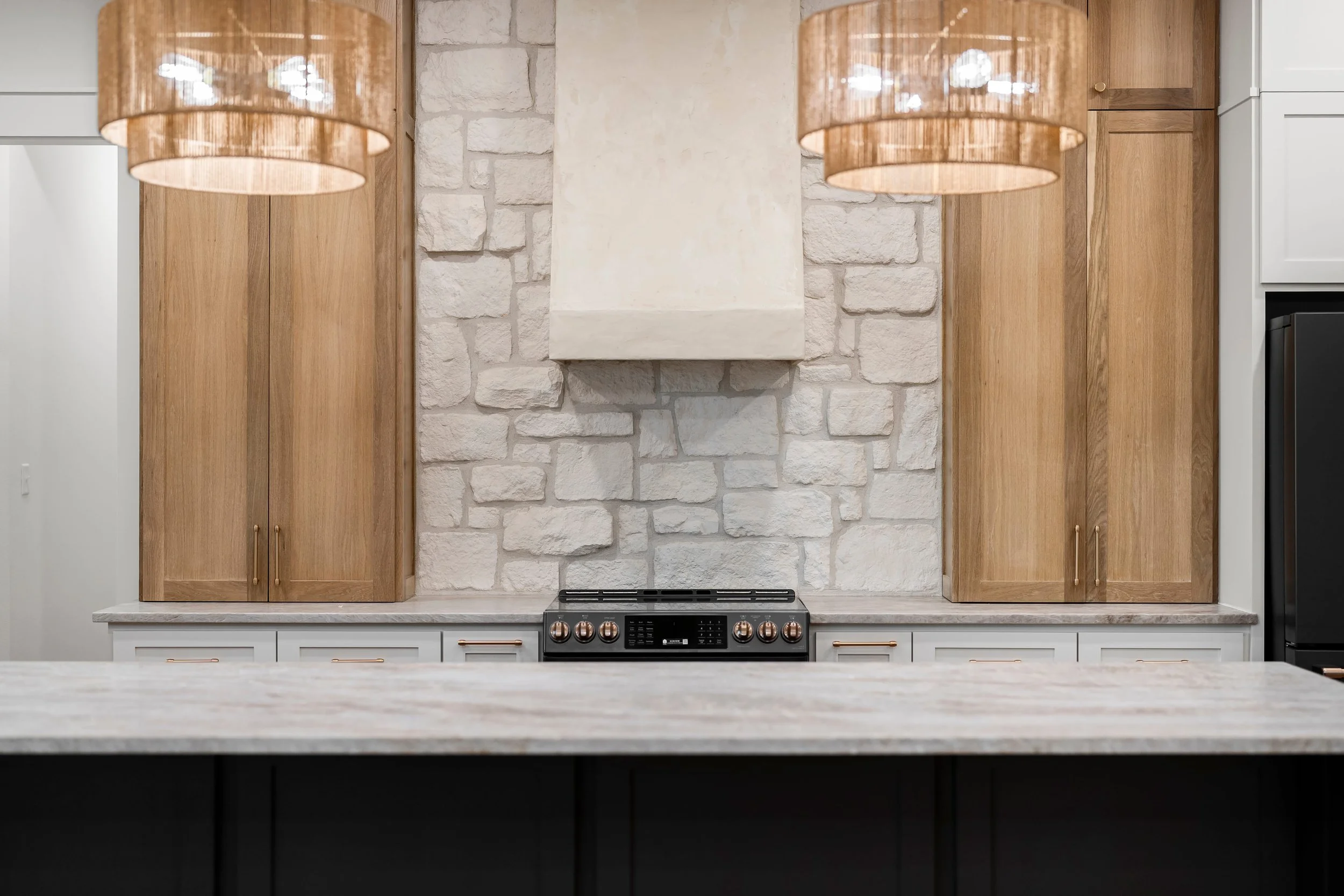 Modern kitchen with light wood cabinets, white brick wall, black stove, and two hanging pendant lights.