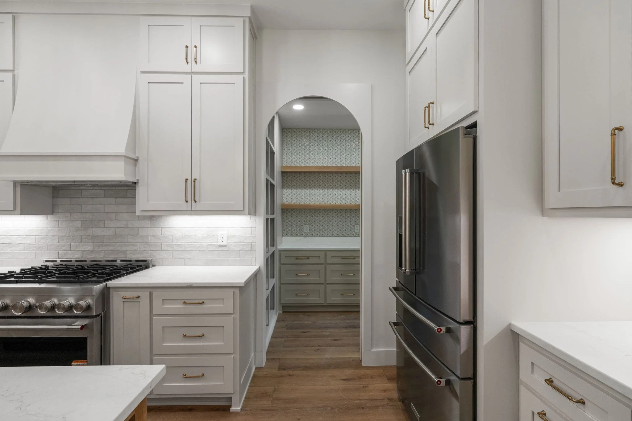 Kitchen with white cabinets, a stainless steel oven and refrigerator, a white countertop, and built-in shelves with wallpapered background.