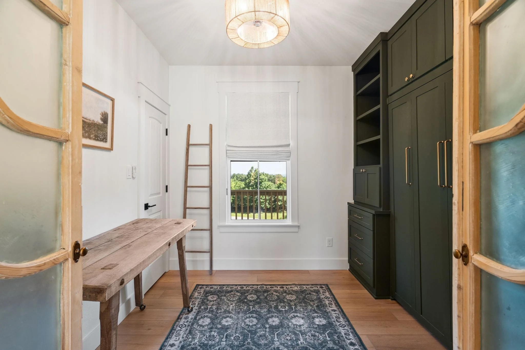 Home office with dark built-in cabinetry, wood desk, patterned rug, and window overlooking the backyard.