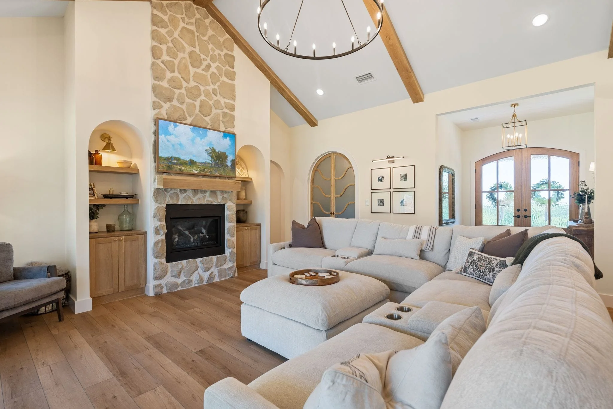 Bright living room featuring a floor-to-ceiling stone fireplace, modern chandelier, and arched wood accent doors.