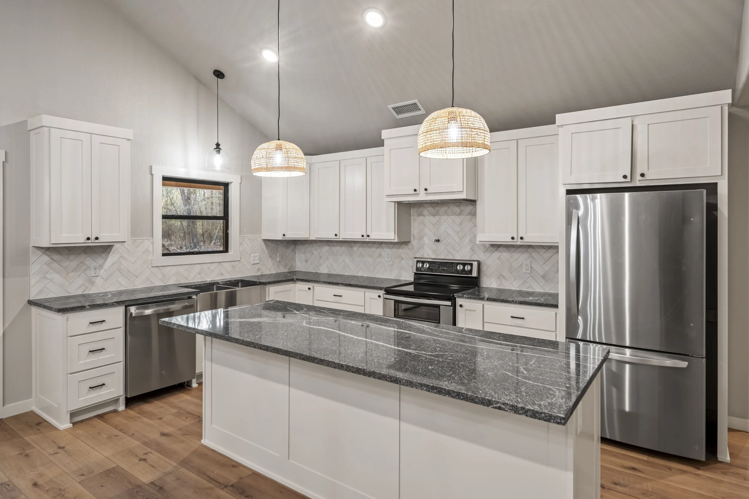 Modern kitchen with white cabinets, dark gray granite countertops, stainless steel appliances, and two woven pendant lights over an island.