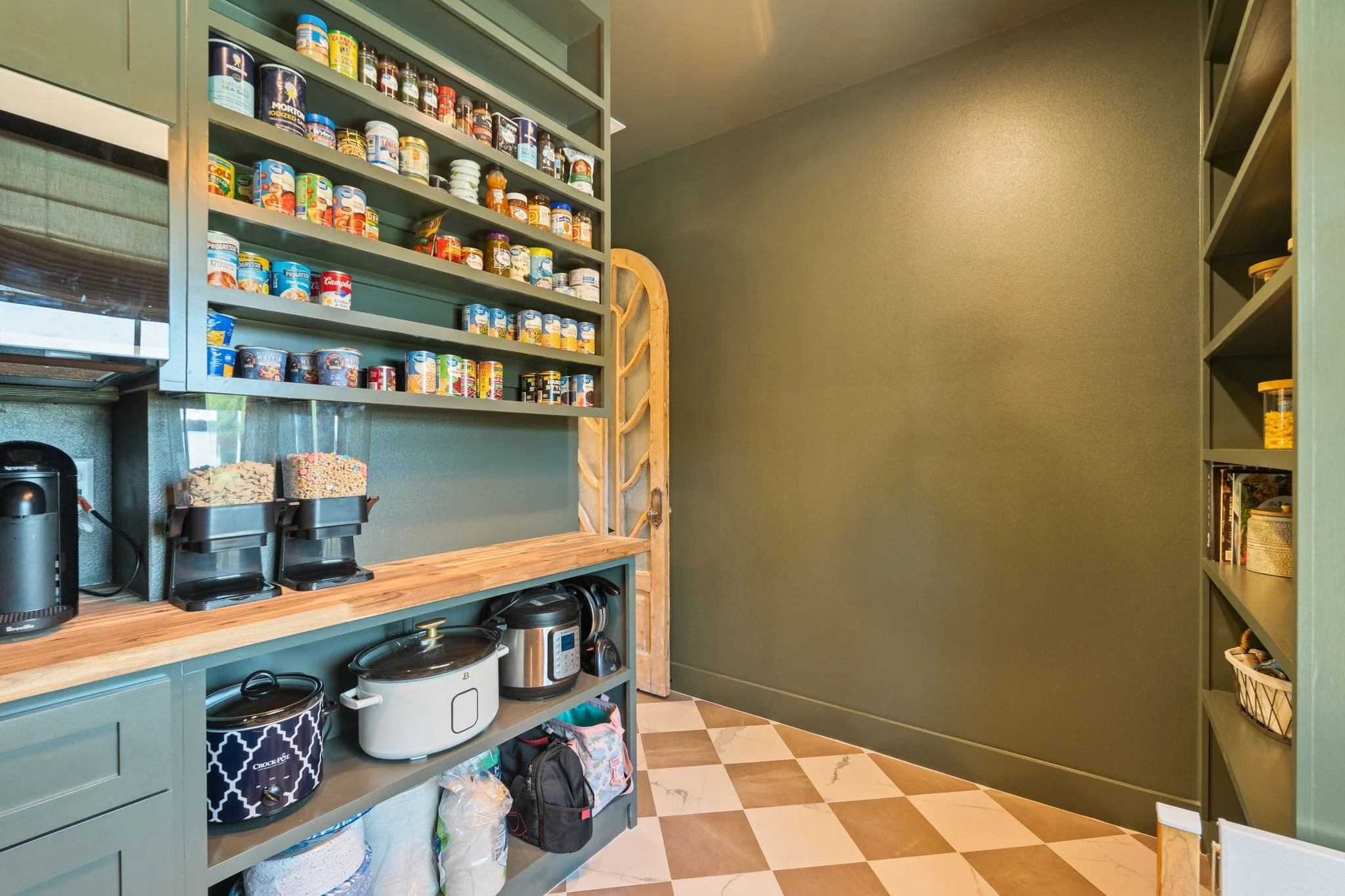 Walk-in pantry with green built-in shelving, checkered tile flooring, and organized food storage.