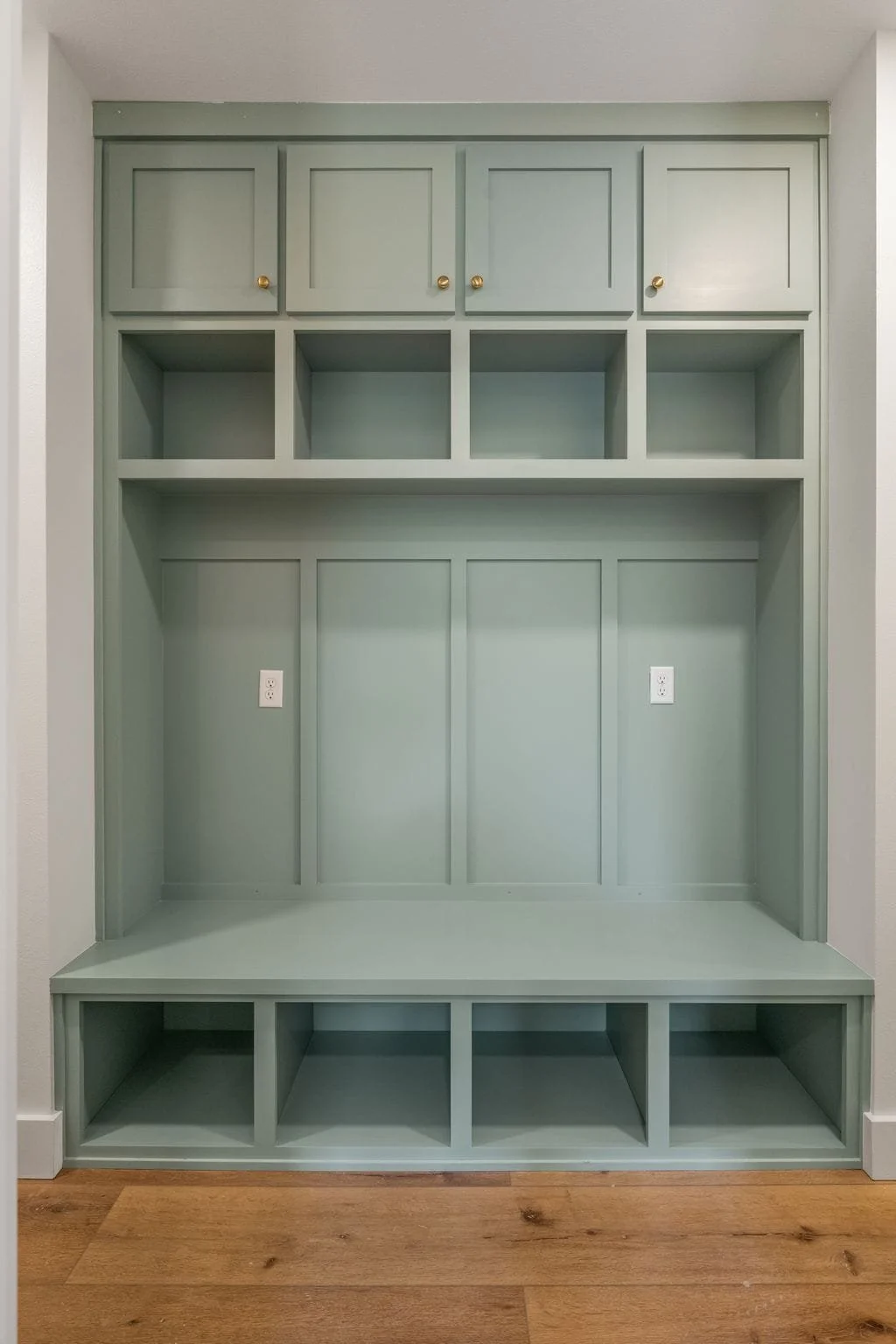Custom built-in mint green storage unit with upper cabinets, open cubbies, a large middle space, and lower compartments, located in a room with hardwood floors.