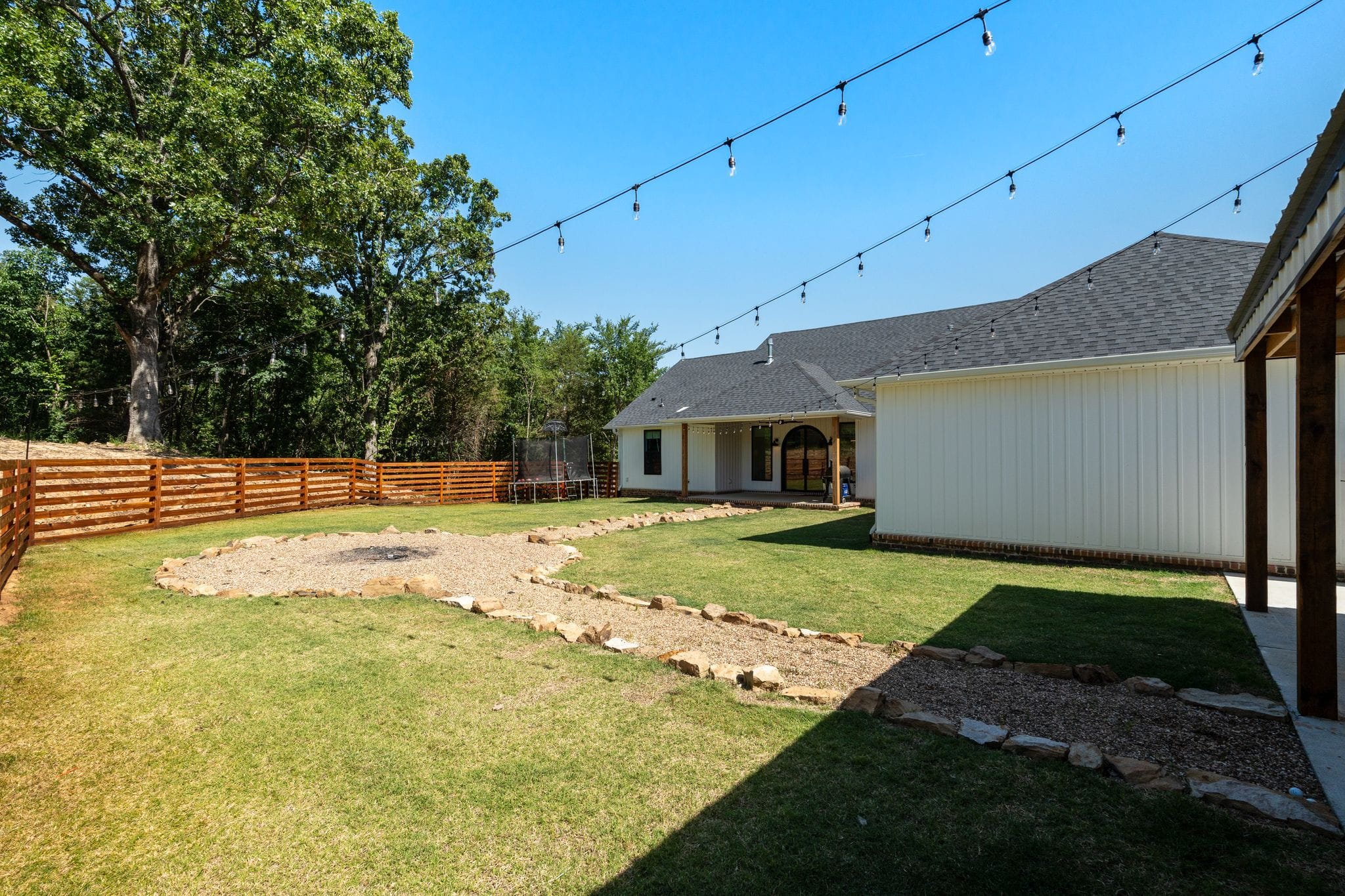 Backyard view of custom farmhouse with fire pit area, string lights, and fenced yard