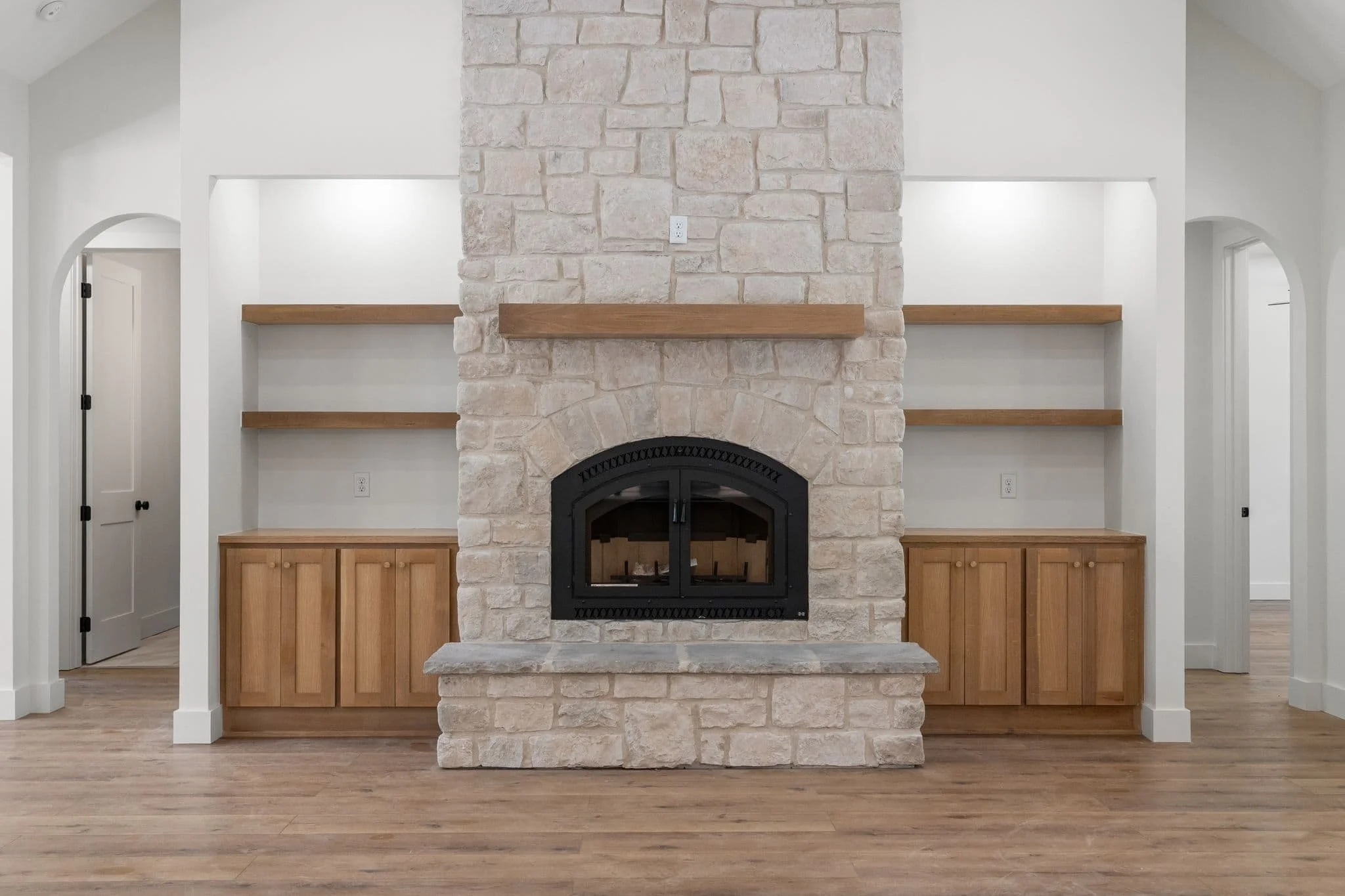 Living room with a large stone fireplace, wooden shelves on either side, and light hardwood flooring.