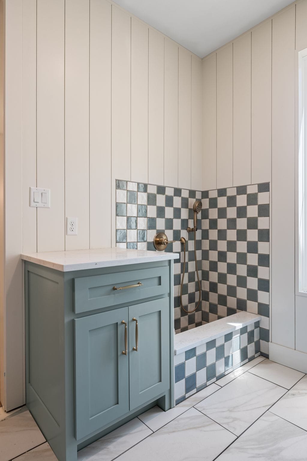 Bathroom with light beige vertical panel walls, a walk-in shower with black and white checkered tile, and a light blue vanity with gold handles.