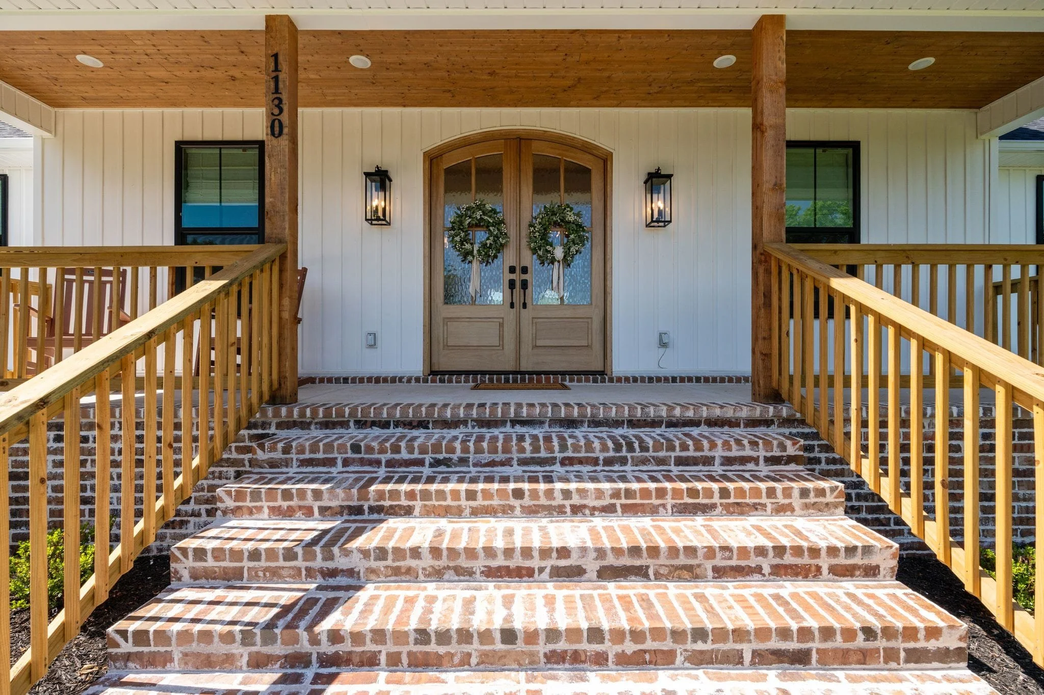 Front porch entrance with brick stairs, wood railings, and decorative wreaths