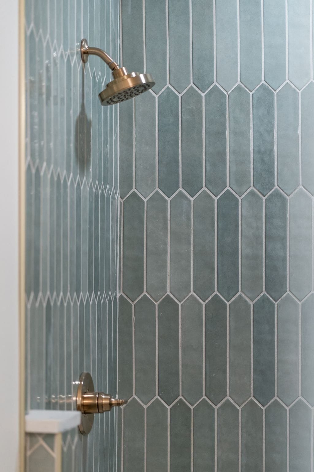 Empty shower with blue hexagonal tiles and a brushed nickel showerhead and control handle.