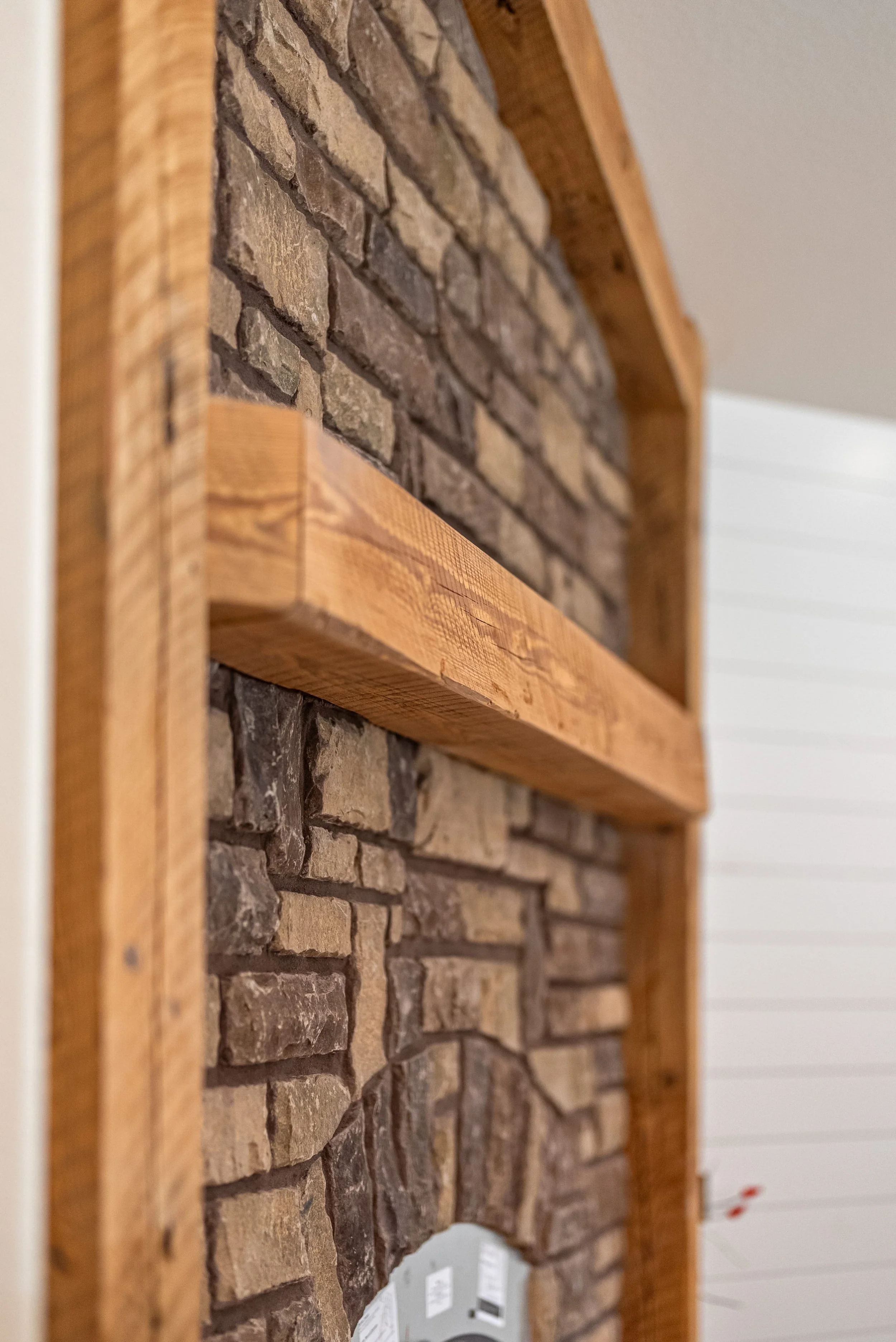 Close-up of a brick wall framed with wooden trim, with a mirror at the bottom reflecting a power outlet and a white shiplap wall.