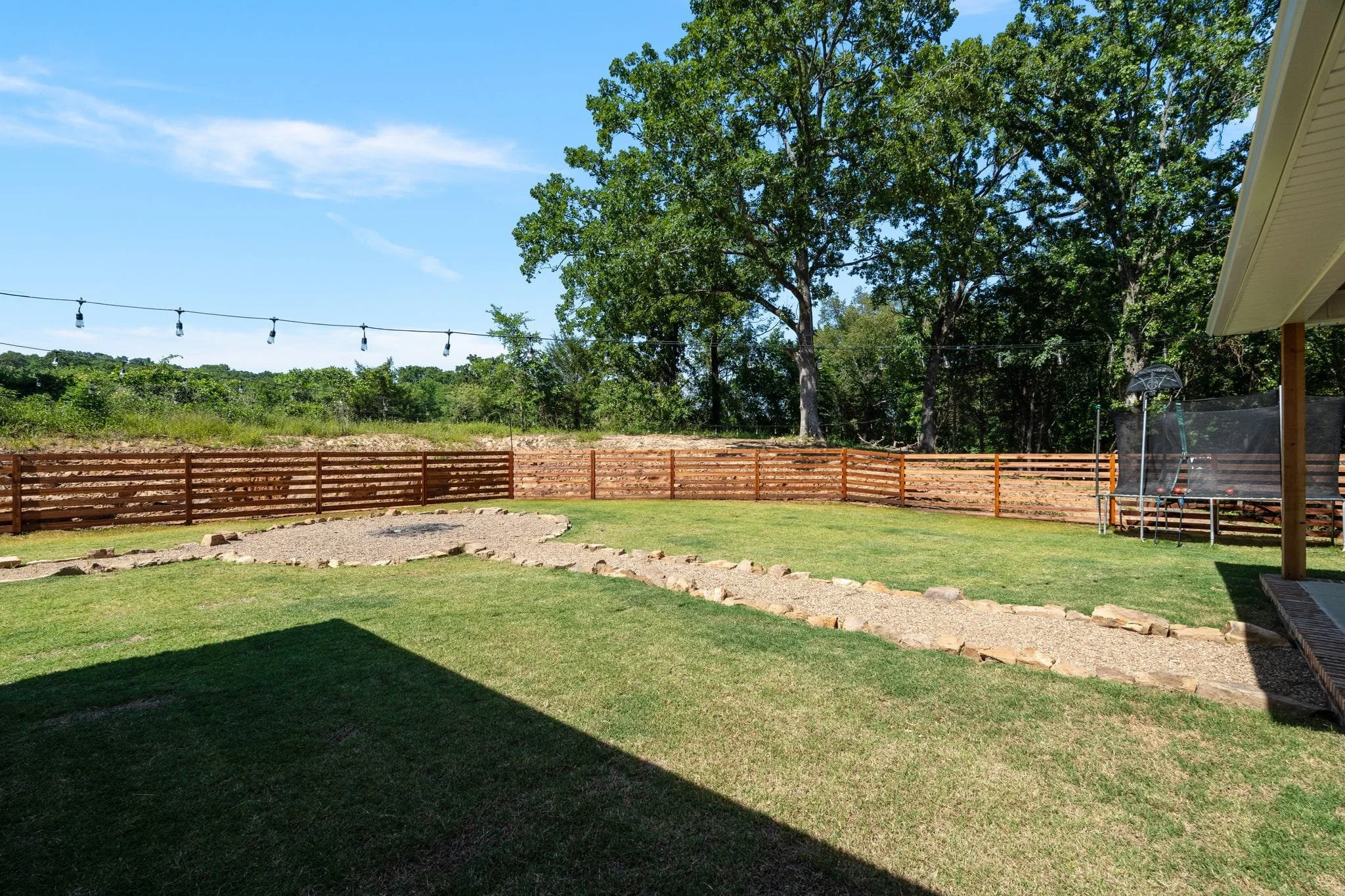 Backyard entertaining area with fire pit, string lights, and fenced lawn