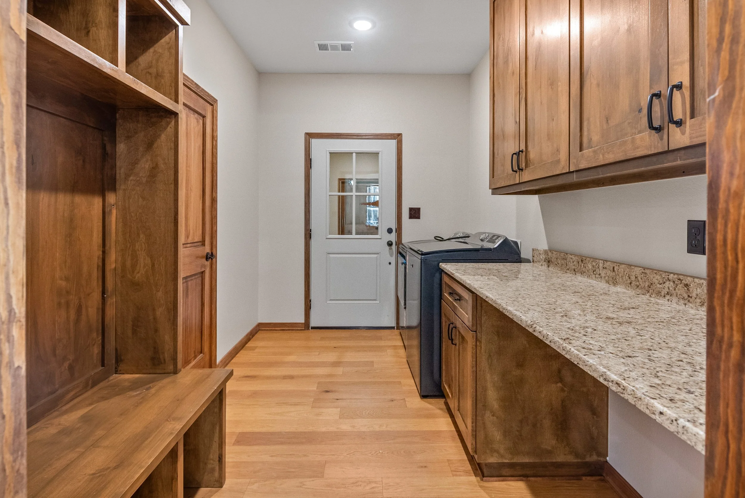 Laundry room with wooden cabinets, granite countertop, washer and dryer, and a door with a window.