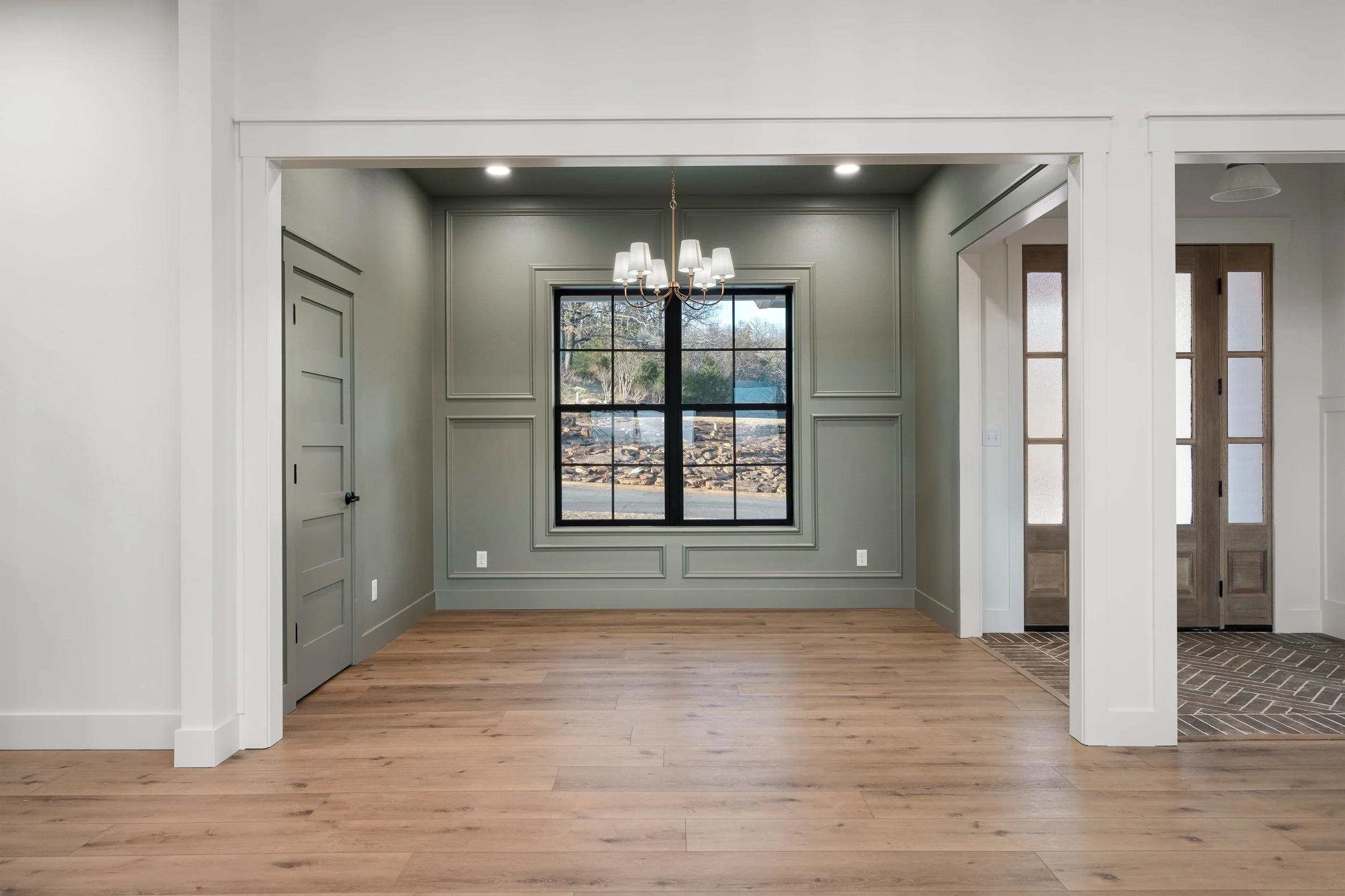 Empty dining room with gray walls, a large window, a chandelier, and hardwood flooring.