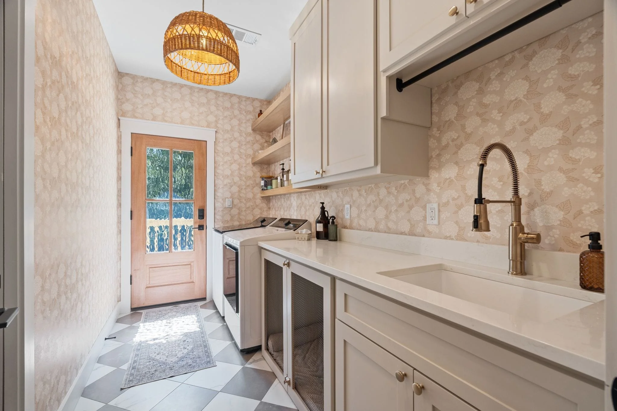 Laundry room with floral wallpaper, custom cabinetry, utility sink, patterned tile flooring, and exterior access door.