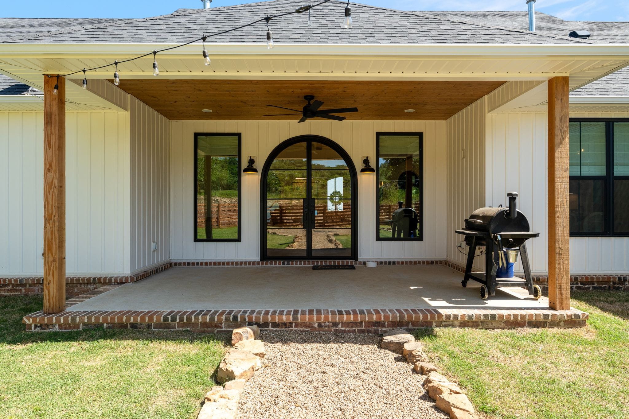 Covered back patio with arched black doors, wood ceiling, and outdoor grill