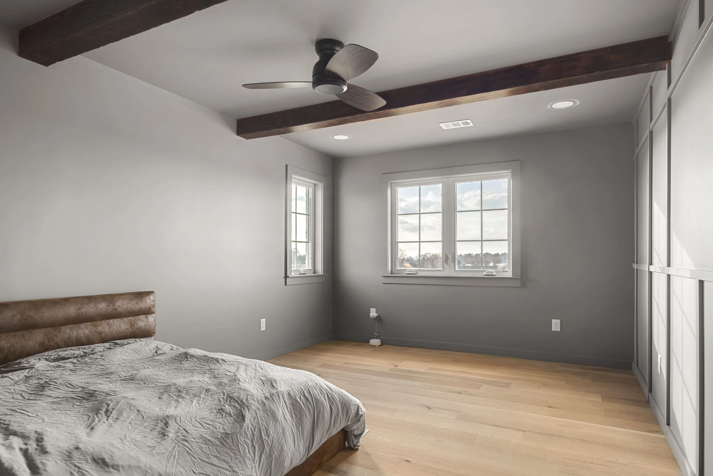 Empty bedroom with a bed, large window, ceiling fan, hardwood floors, and neutral-colored walls.