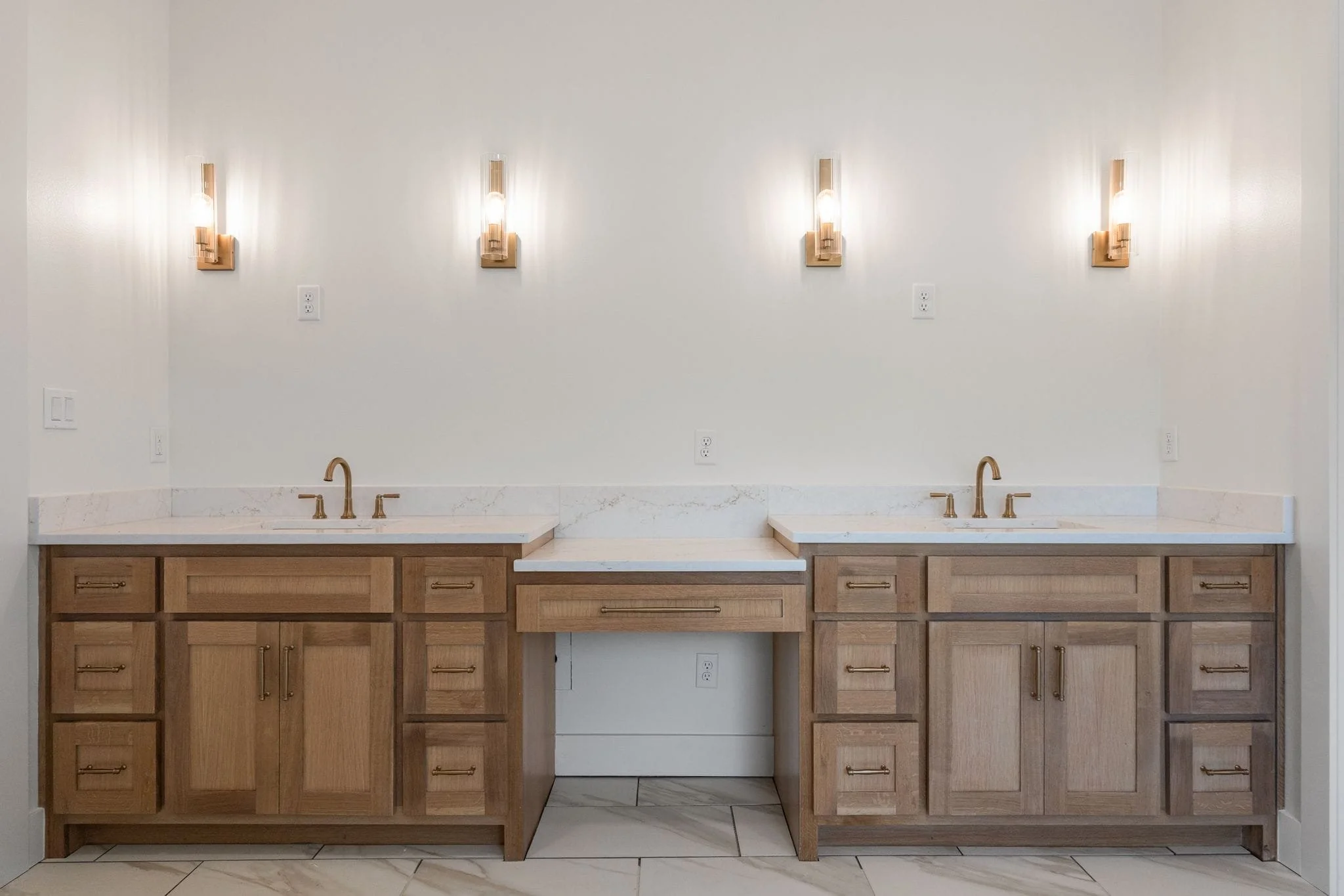 Kitchen with wooden cabinets, two sinks, marble countertops, wall-mounted light fixtures, electrical outlets, and tiled floor.
