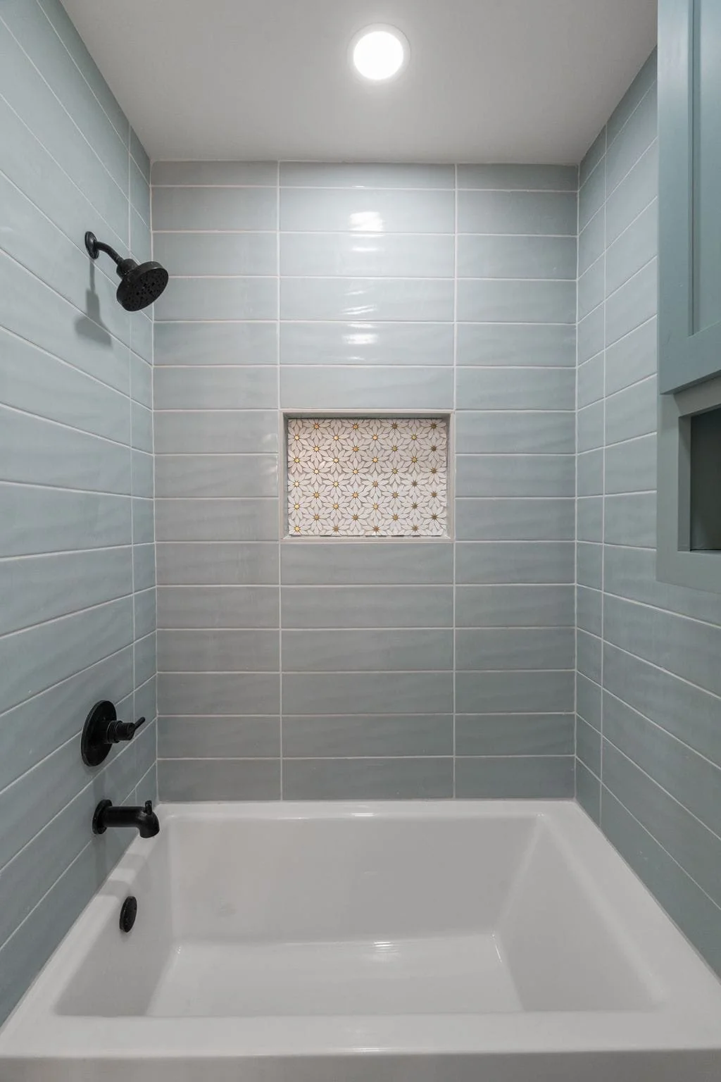 Shower area with gray tiled walls, a black showerhead, and a small decorative tile niche.
