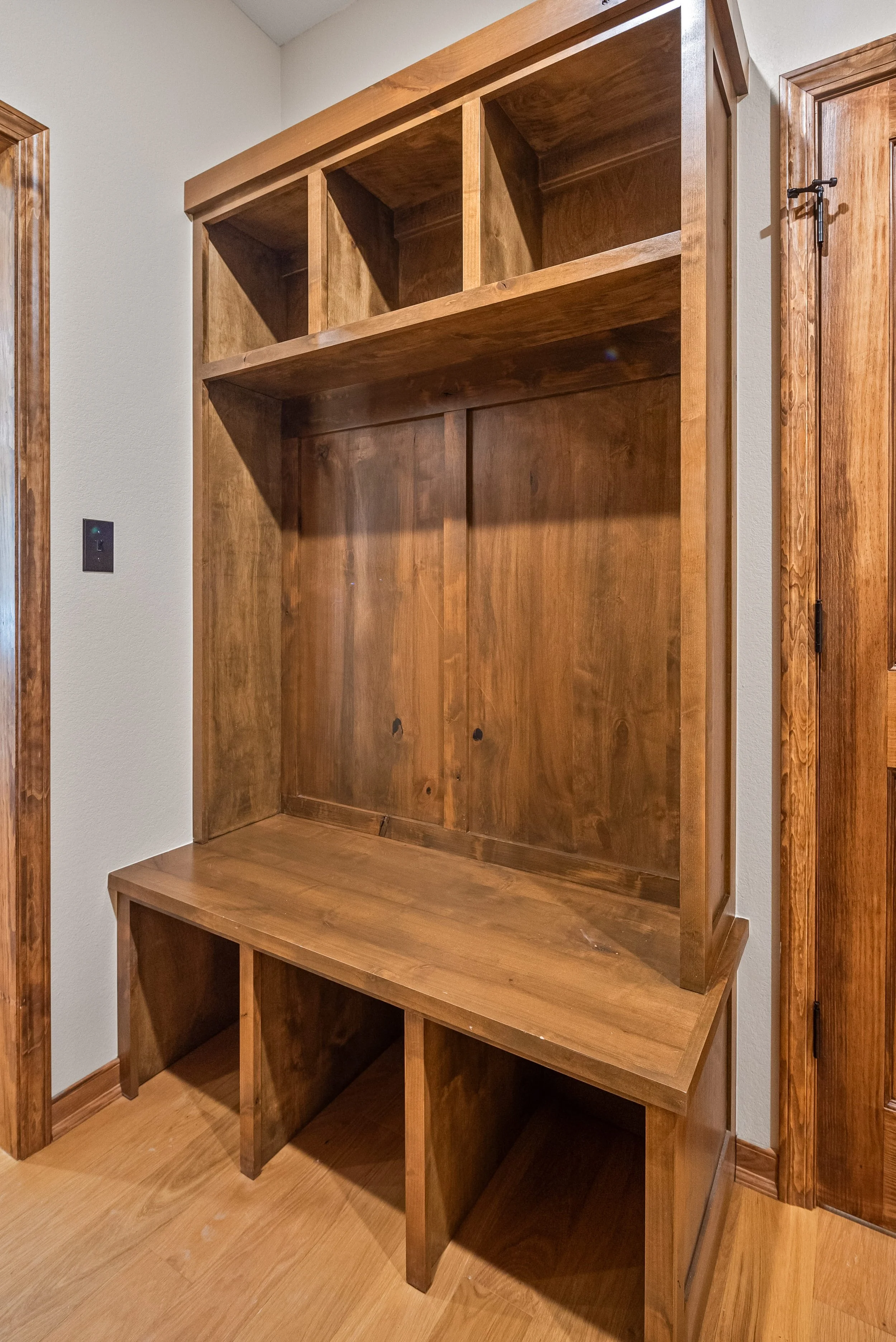 A large wooden bookshelf with multiple open cubbies, placed against a wall in a room with wood flooring.