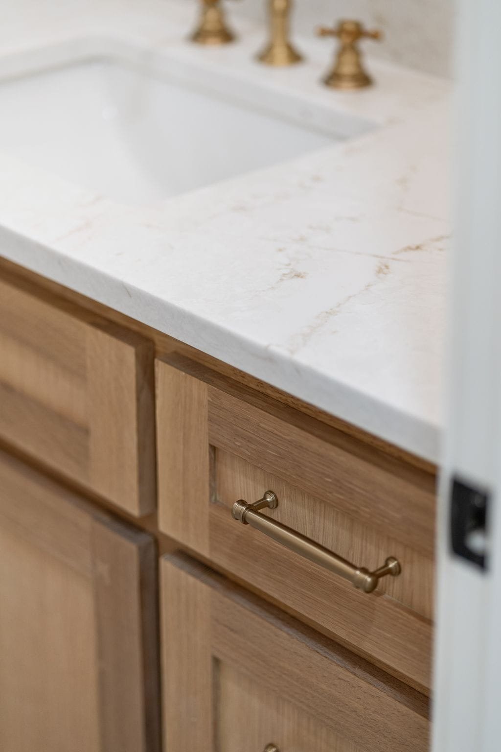 Close-up of a kitchen countertop and wooden cabinet with brass handle, featuring a marble or stone surface and brass faucet fixtures.