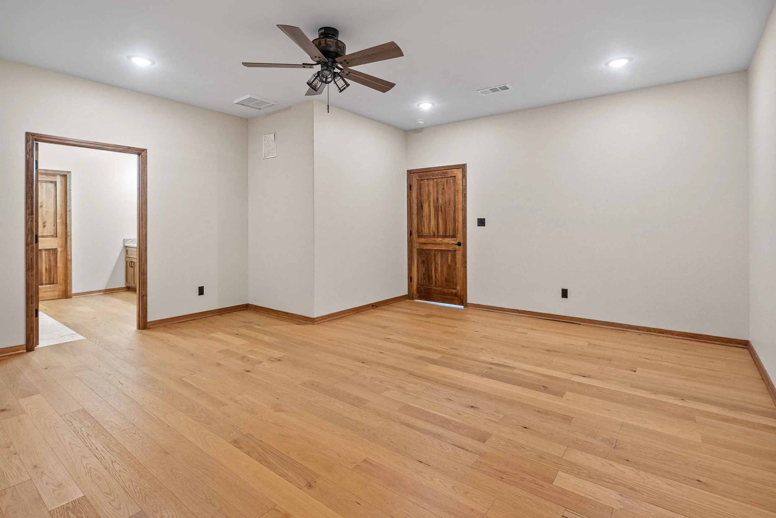 Empty room with hardwood floors, white walls, wooden doors, ceiling fan, and recessed lighting.