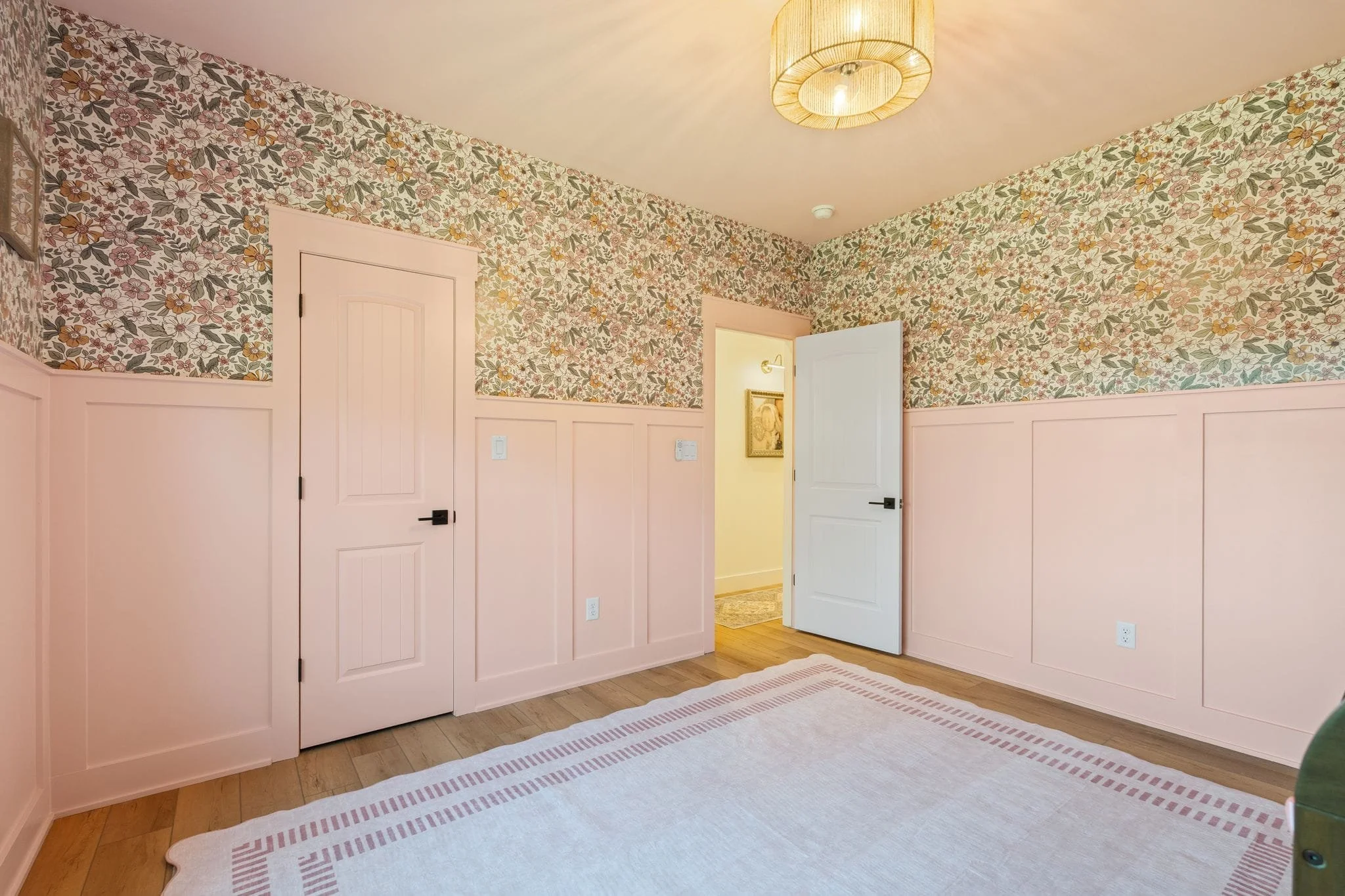 Floral nursery featuring pink trim, decorative wallpaper, soft area rug, and adjoining hallway entrance.