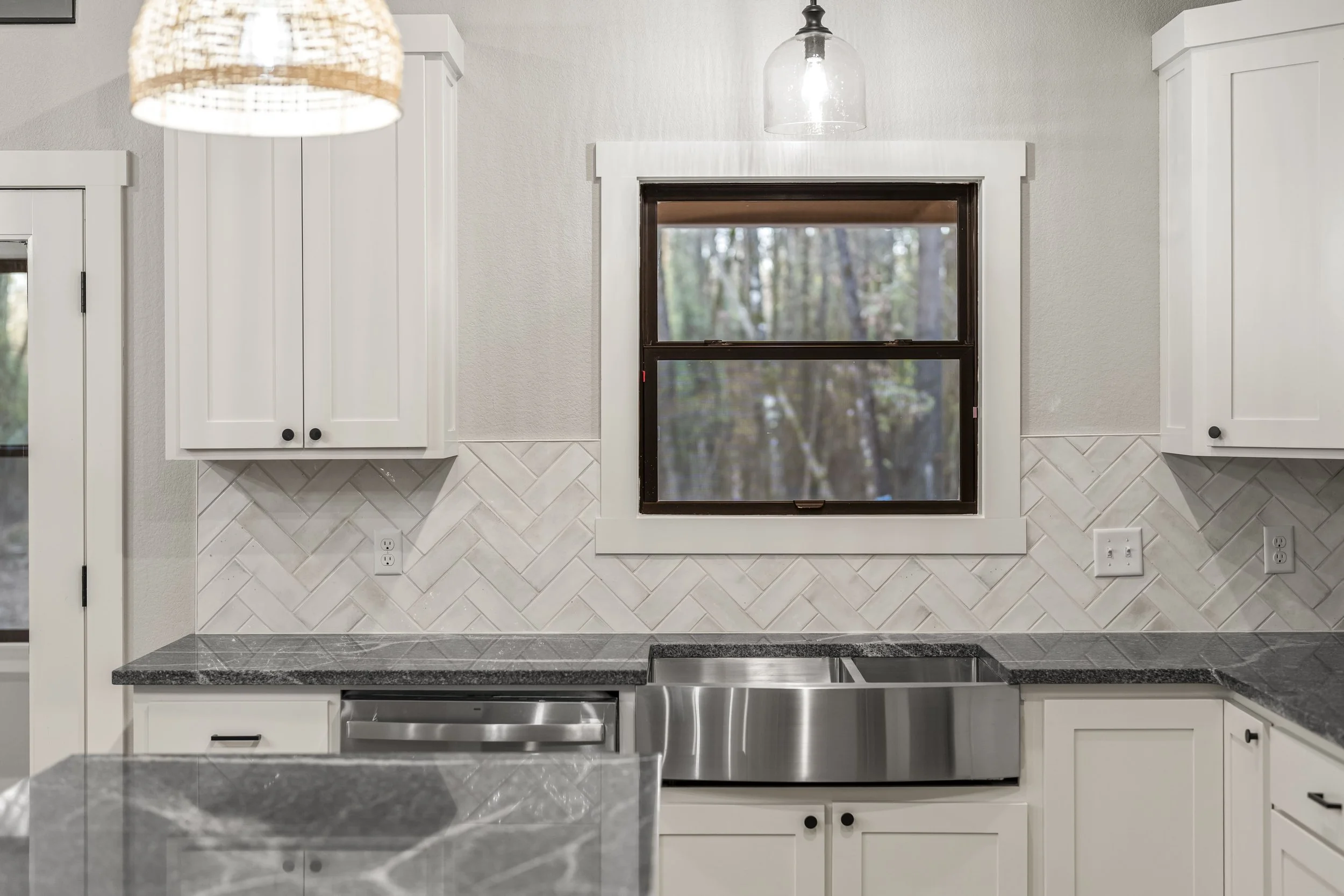 Modern kitchen with white cabinets, a black granite countertop, a stainless steel sink, and a window showing trees outside.