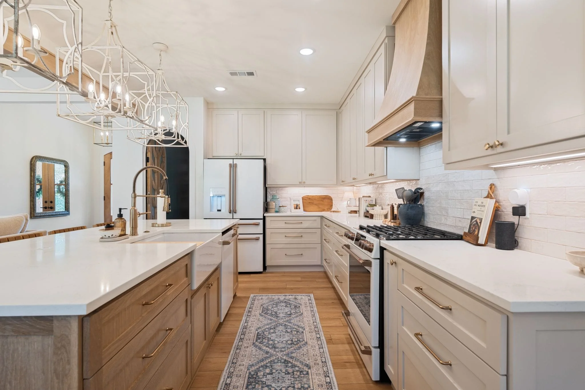 Galley-style kitchen with custom wood vent hood, white cabinetry, gas range, and patterned runner rug.