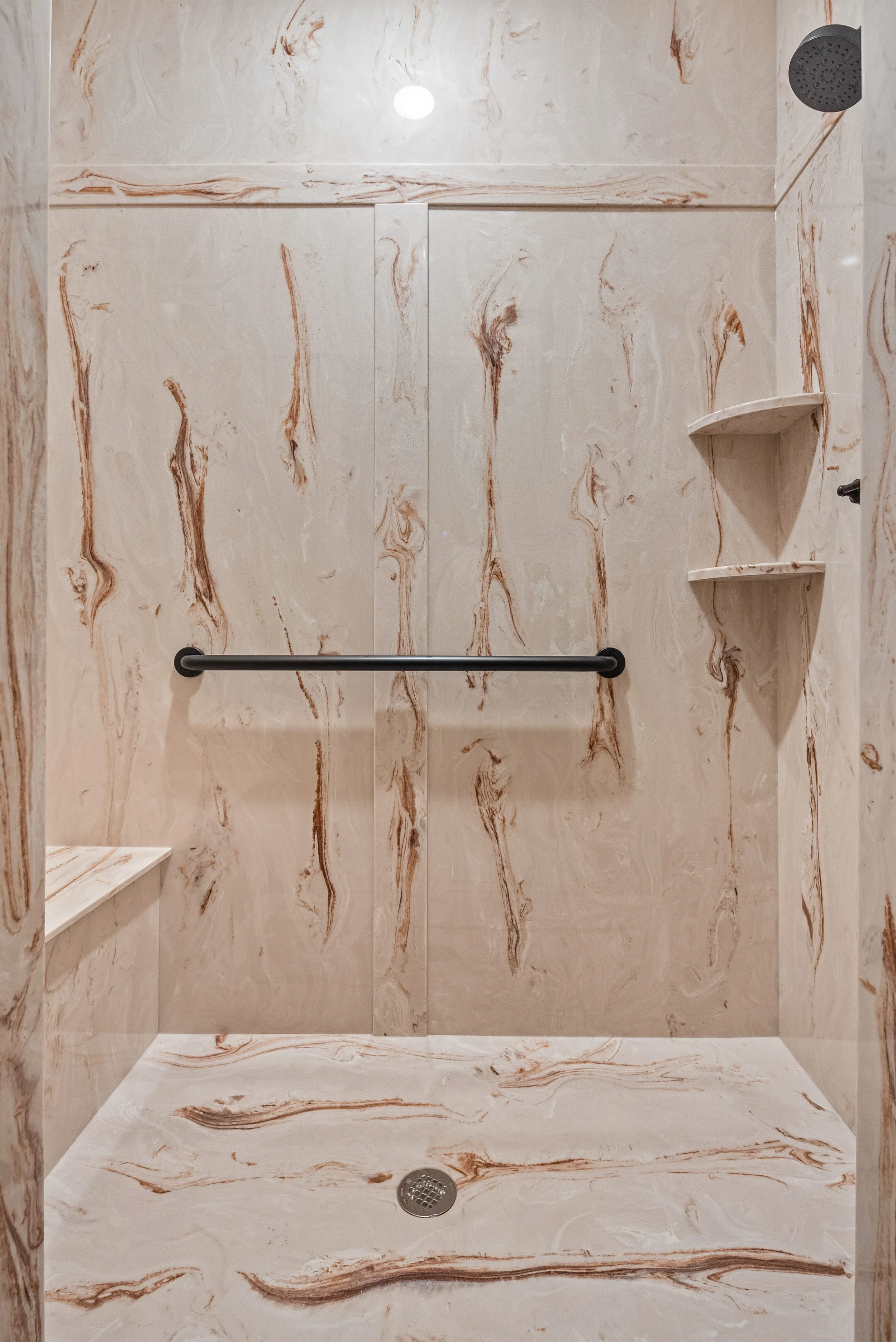 Marble shower with built-in bench, corner shelves, black grab bar, and rain shower head.