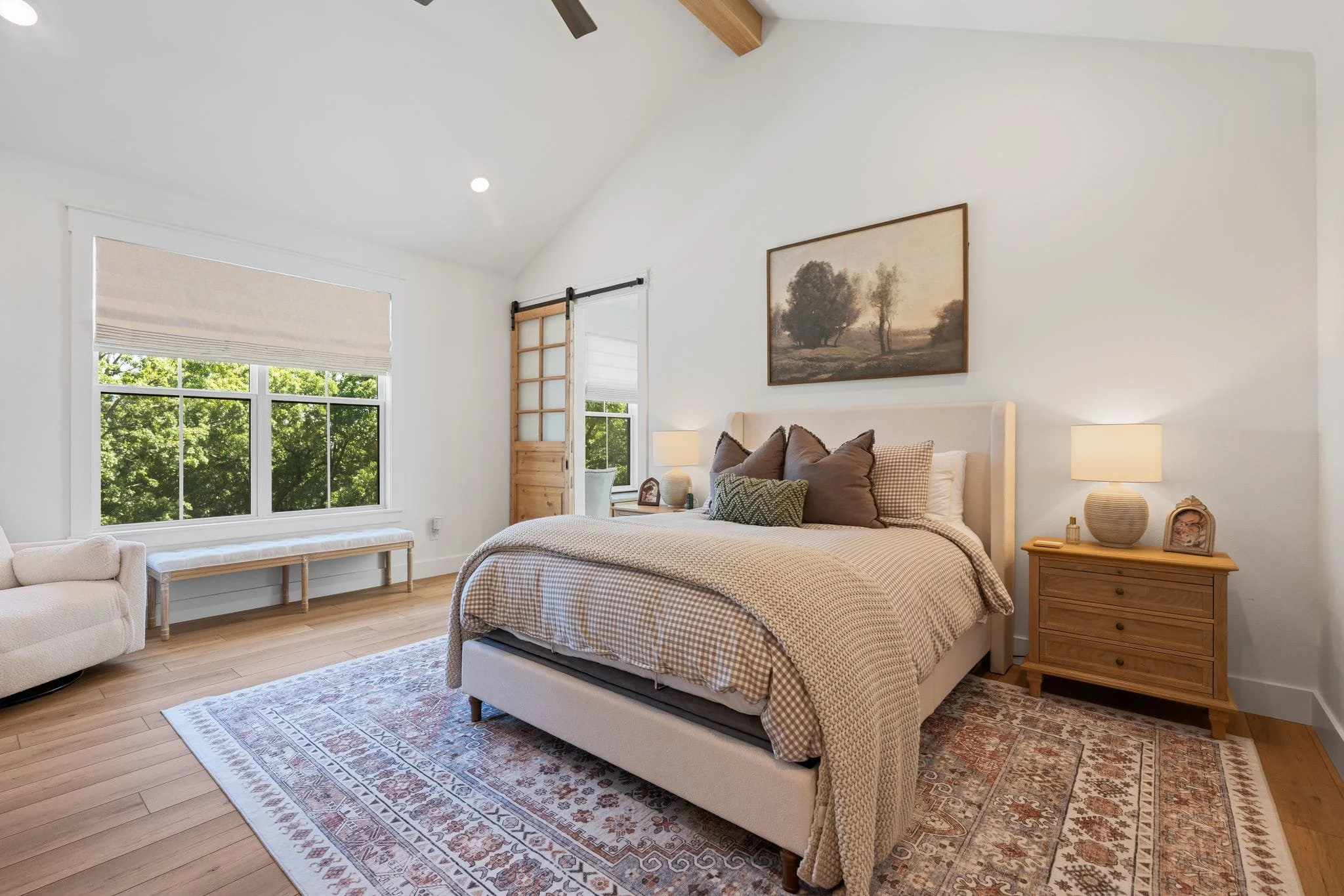 Spacious primary bedroom with vaulted ceiling, upholstered bed, patterned rug, and sliding barn door.