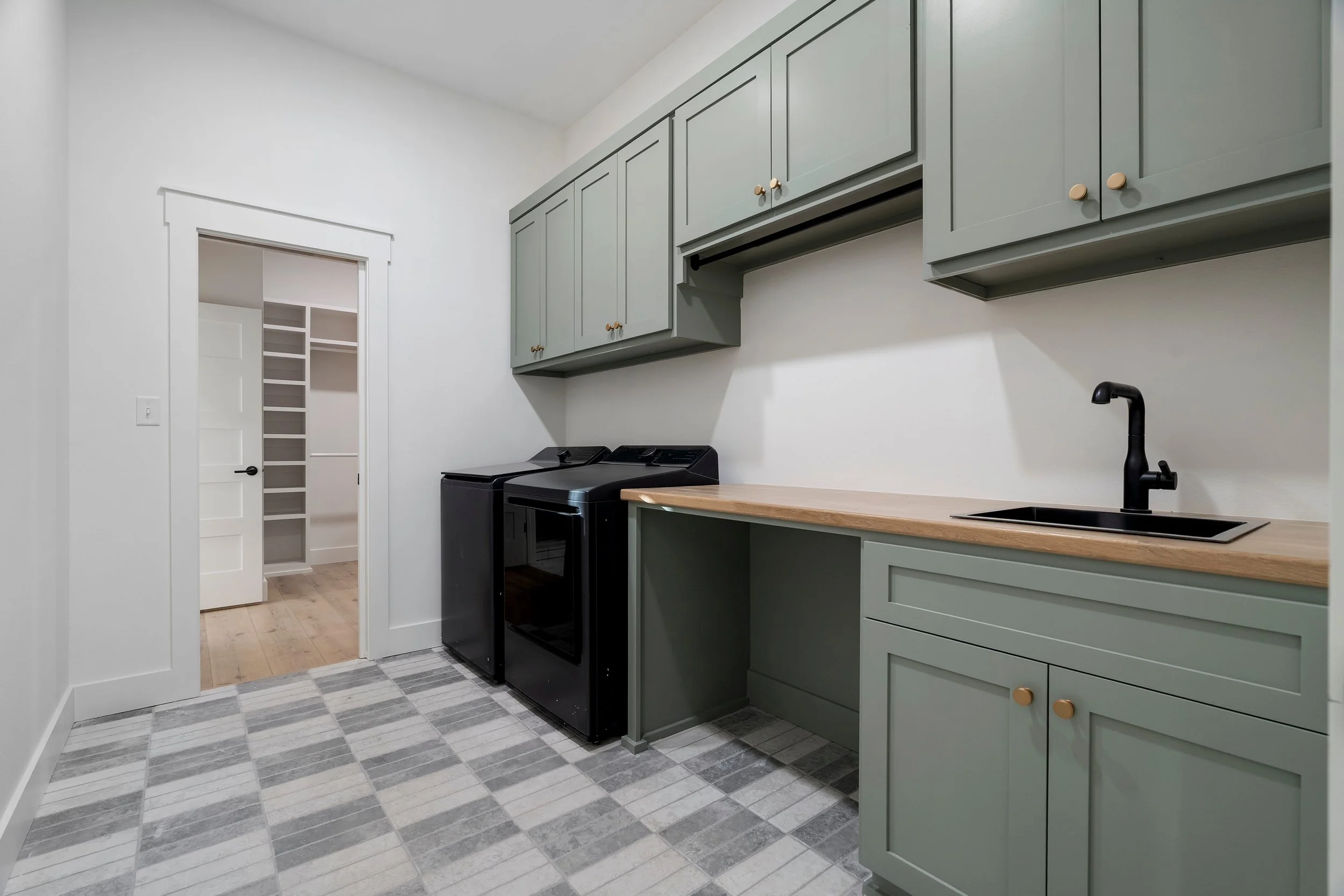 Laundry room with green cabinets, black washer and dryer, wooden countertop, black sink with faucet, and sliding door leading to a walk-in closet.