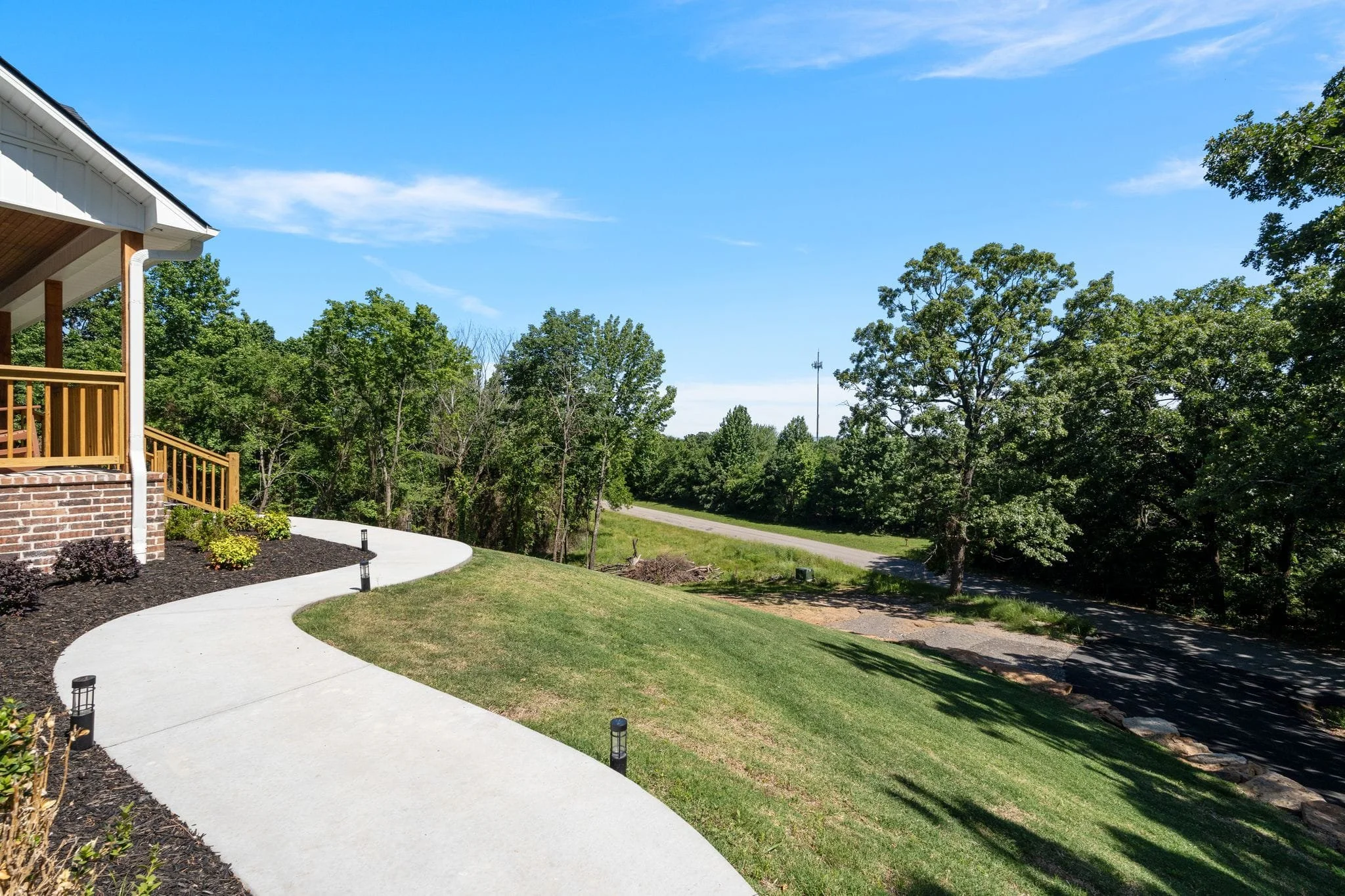 Curved concrete walkway beside landscaped front yard and wooded property view