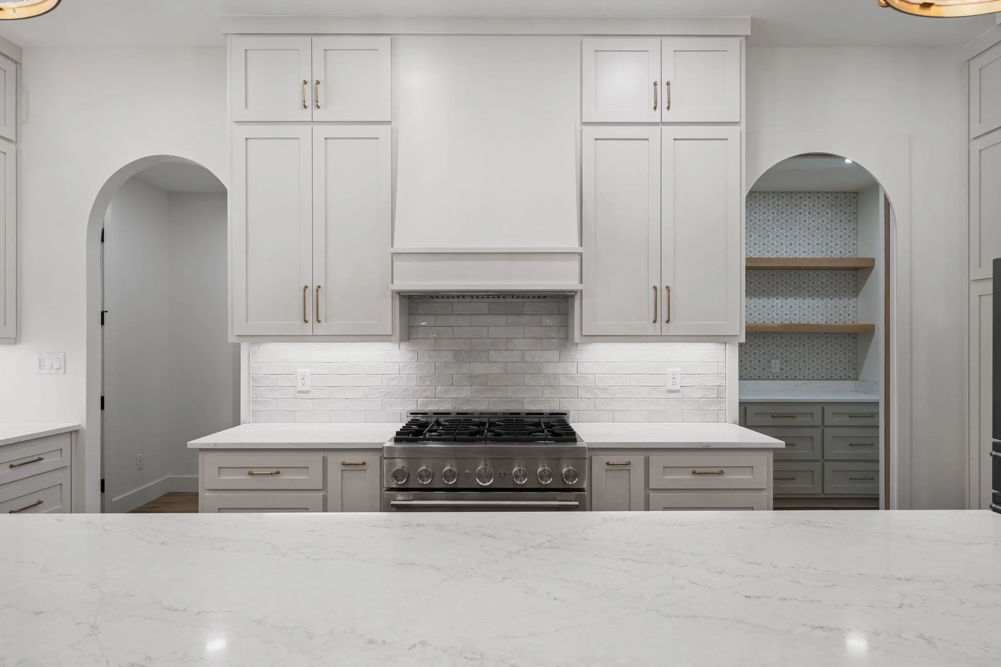 Modern kitchen with white cabinets, gray backsplash, stainless steel stove, and white marble countertops.