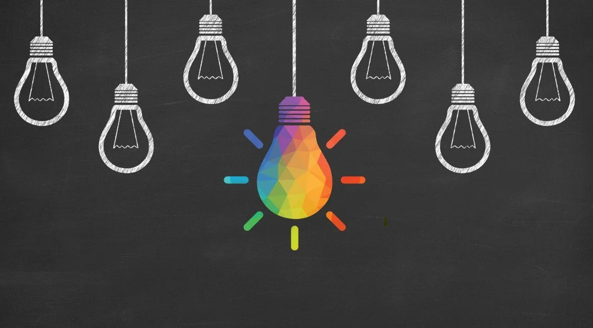 Drawing of illuminated light bulbs on a black chalkboard background, with one colorful, rainbow-colored light bulb in the center.