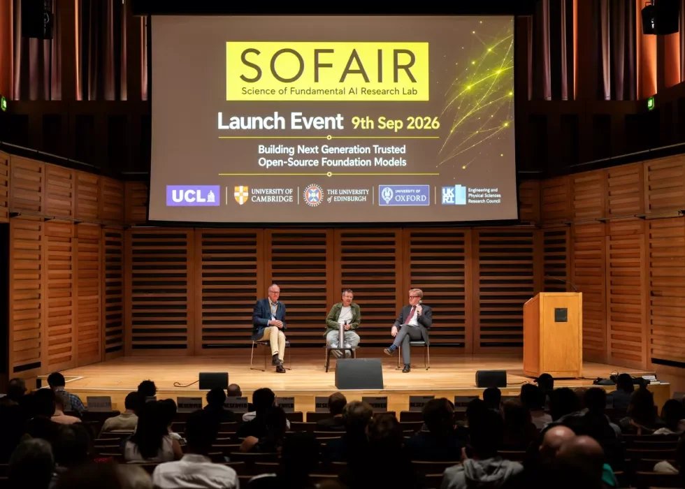 Pictured is a stage with three men having a discussion about evolving AI technologies. There is a large banner above their heads
