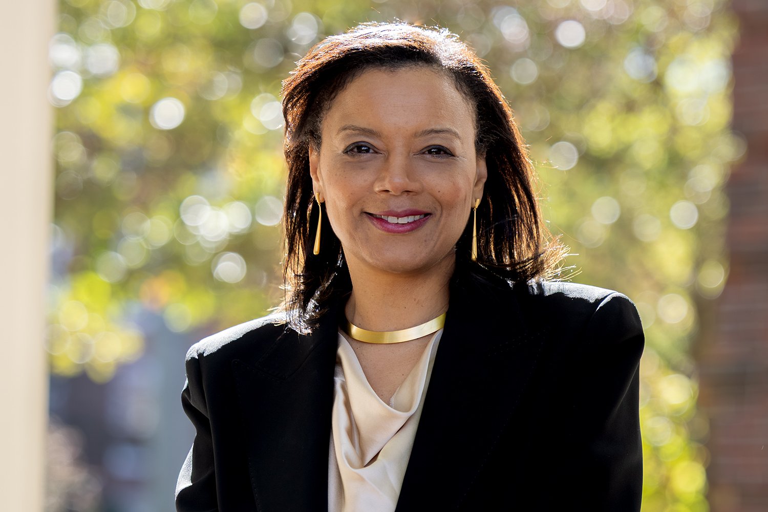 Tomiko Brown-Nagin smiling outdoors in a black blazer and gold necklace
