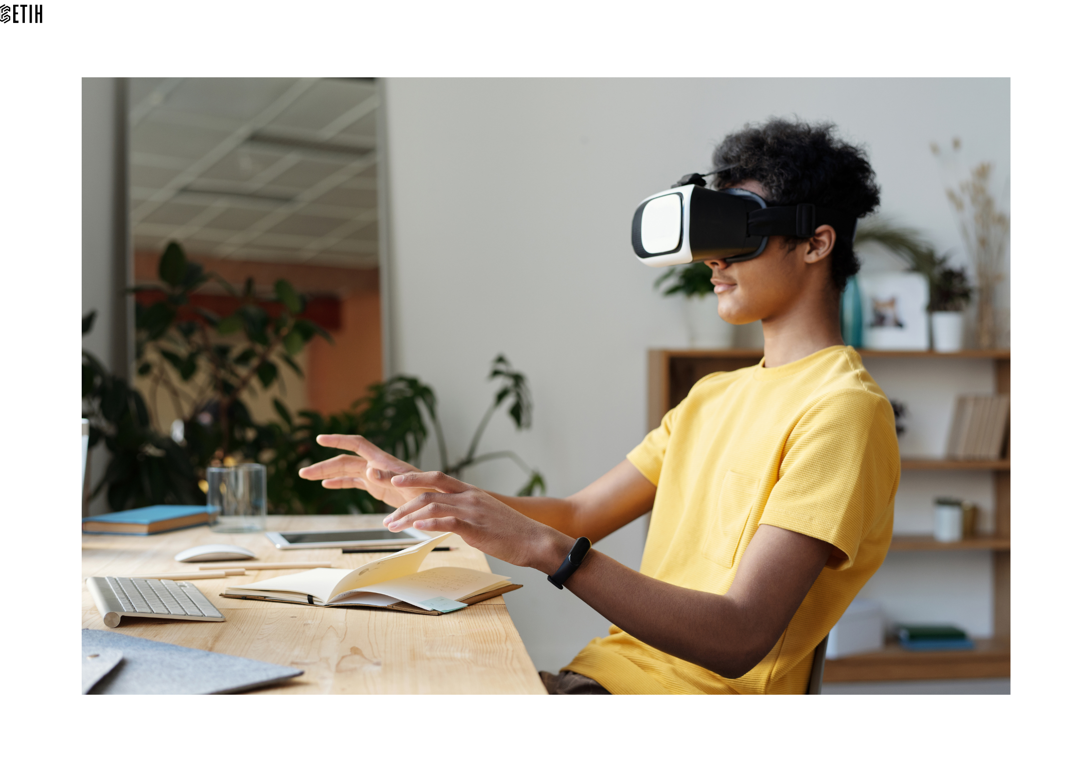 Pictured is a male student, wearing a yellow T-shirt, sitting at his desk with a notebook and computer keyboard, and wearing a virtual reality headset