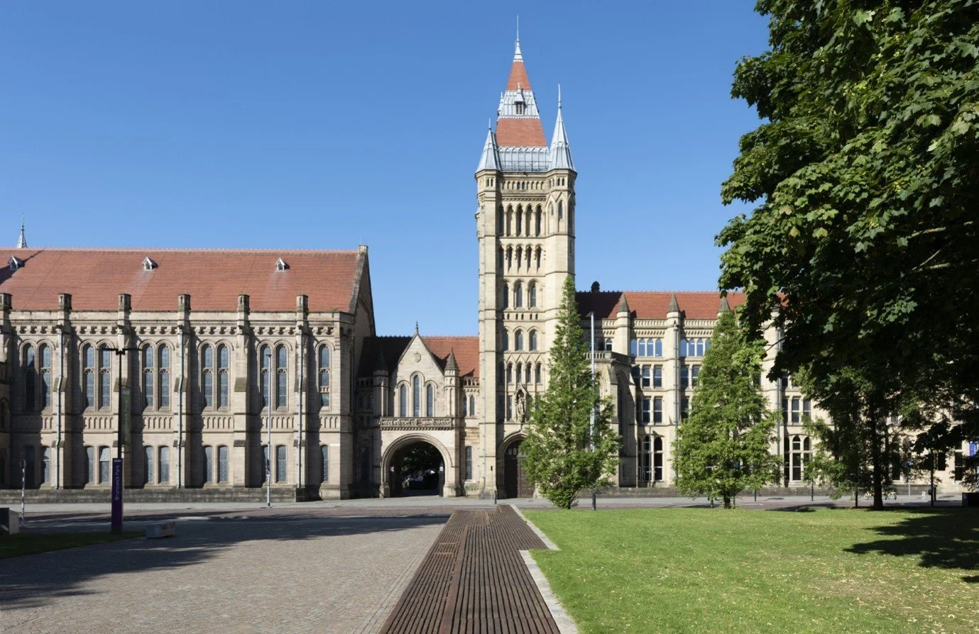 Pictured is an image of Mancester University, including trees, a lawn and a tower