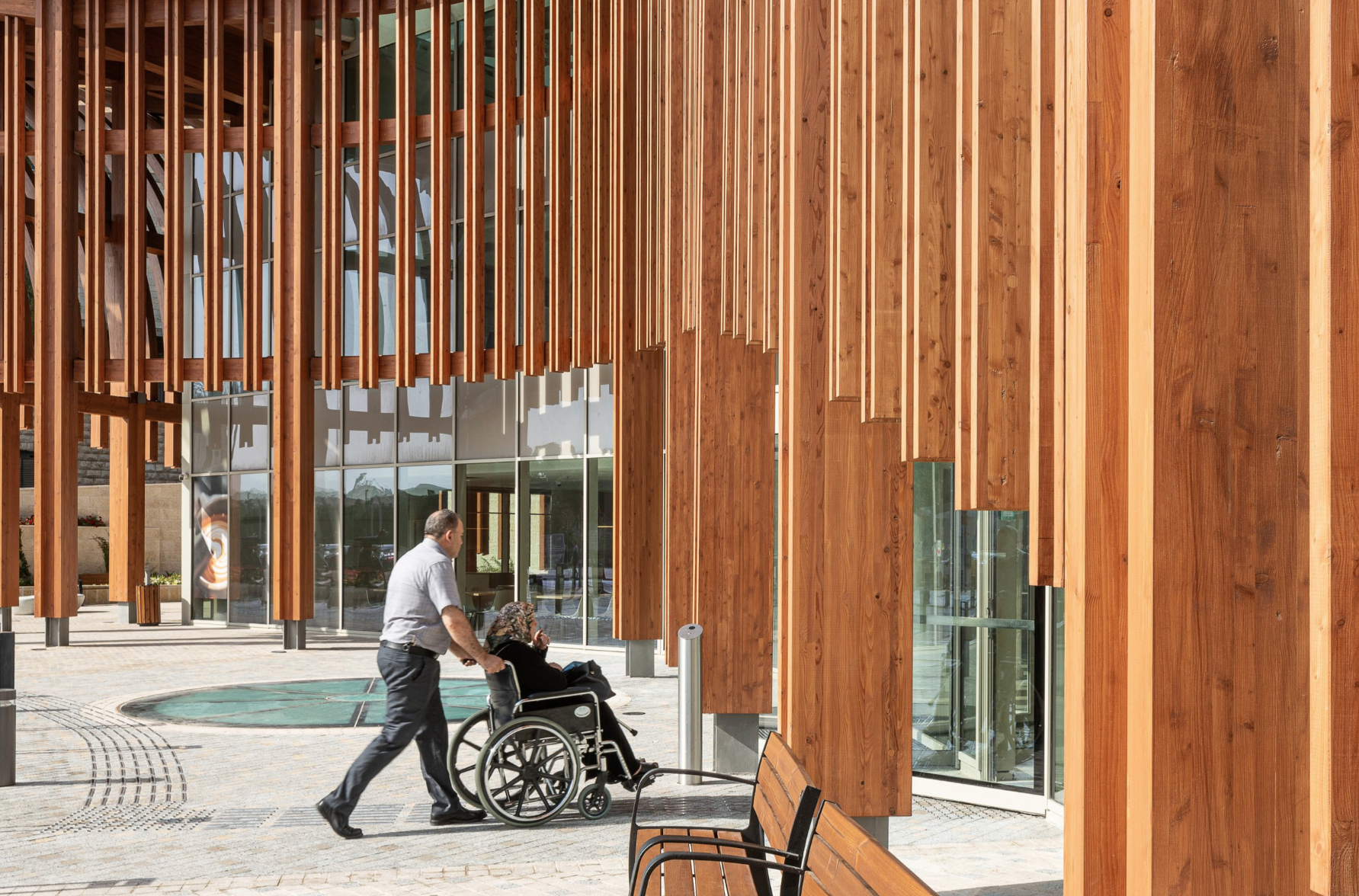 Wooden colonnade outside the Helmsley Cancer Center with a person in a wheelchair passing by, showcasing inclusive, human-centered architectural design.
