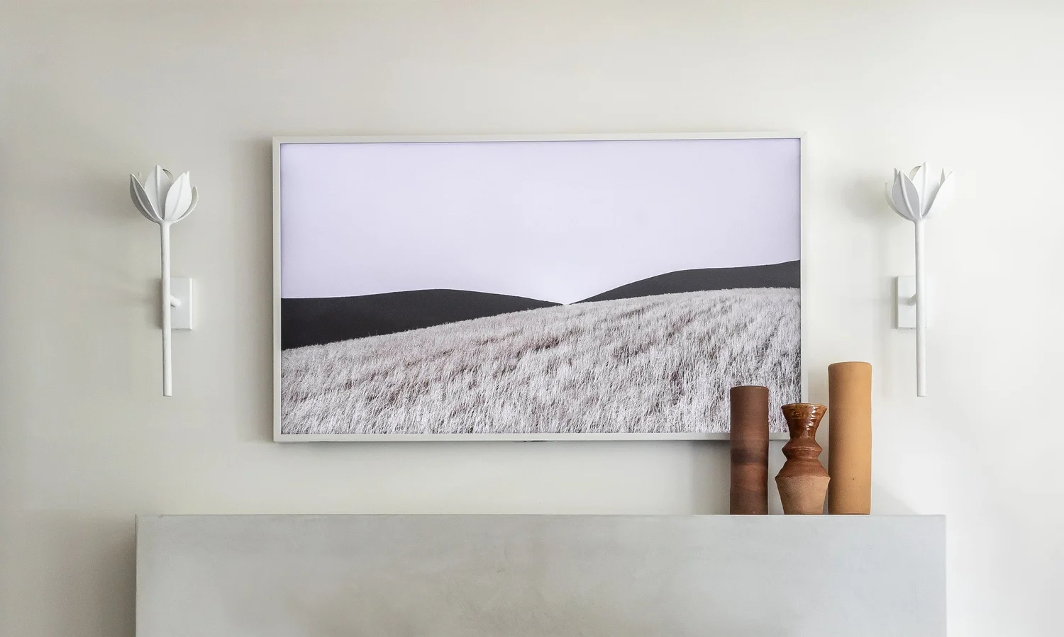 A Dayhouse Studio living room: a framed landscape above a plaster mantel, flanked by sculptural wall lights, with ceramic vessels in clay tones.