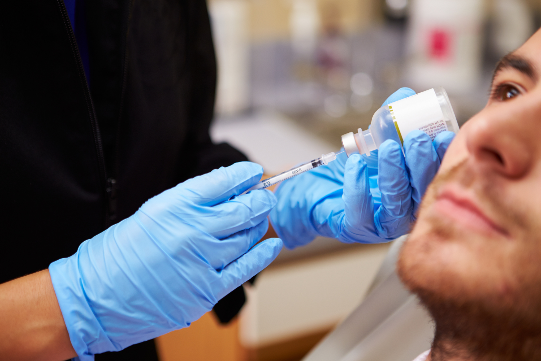 Medical professional in blue gloves preparing a facial injection for a male patient at a dermatology office