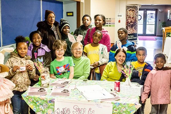 MWA volunteers wearing bunny ears seated with a dozen children at a Spring Brunch Event