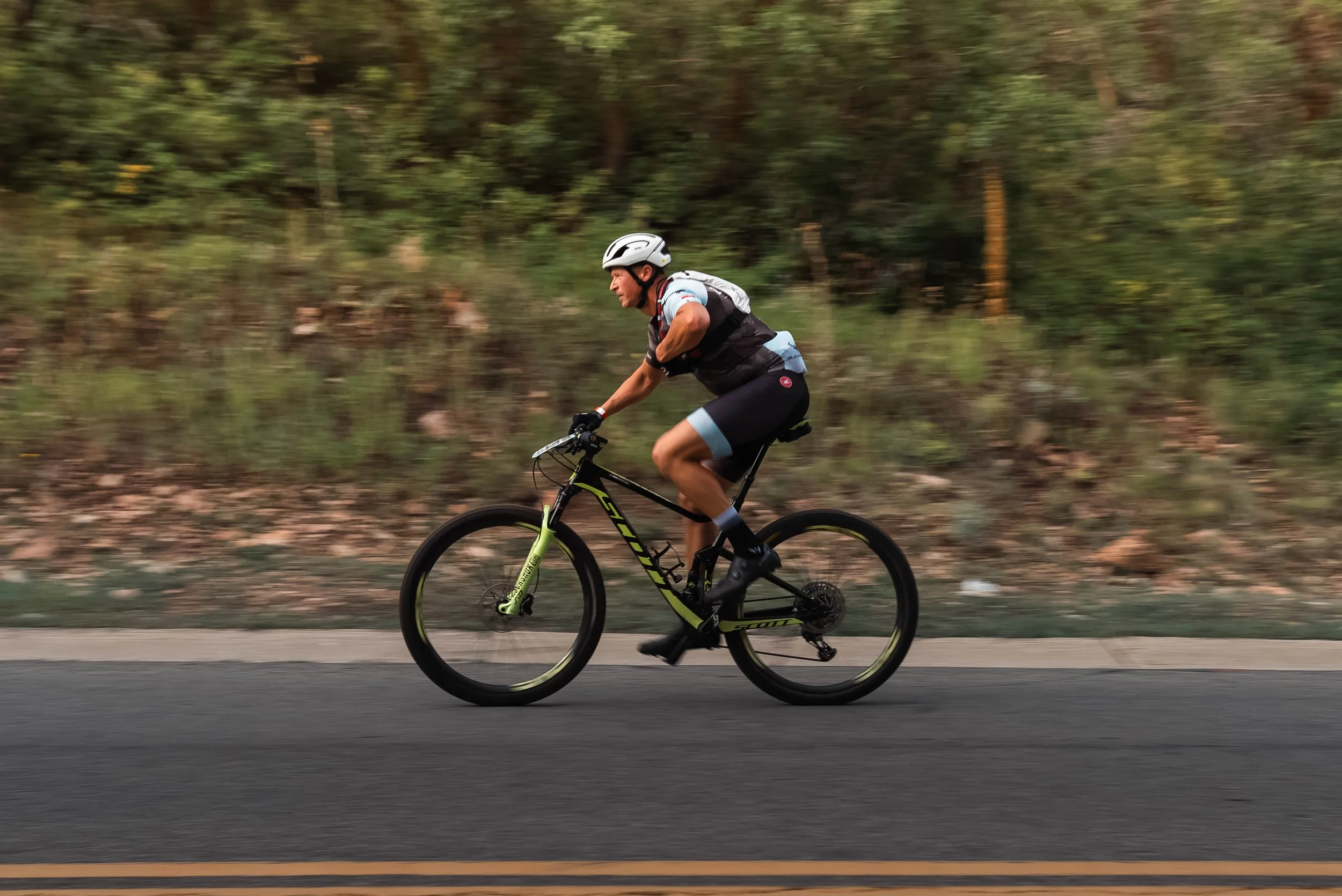 A gravel biker pedaling on a road with a greenery behind at the Point to Point race in Park City, Utah.