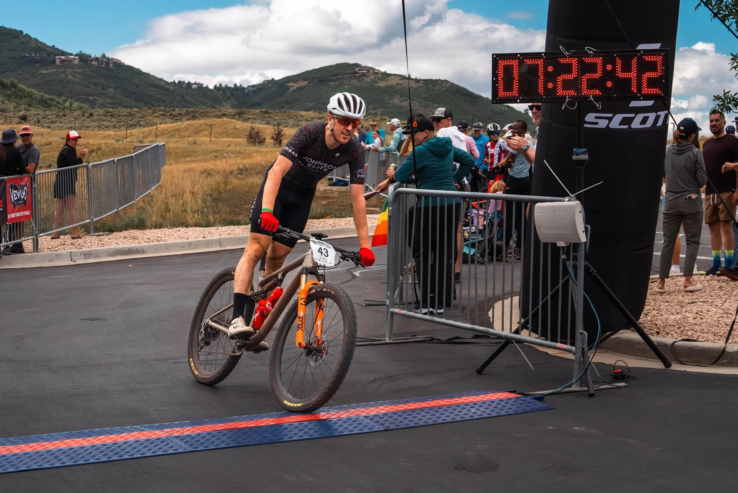 Biker going through the finish line at Skullcandy in Park City, Utah for the Point to Point race with mountains behind him.