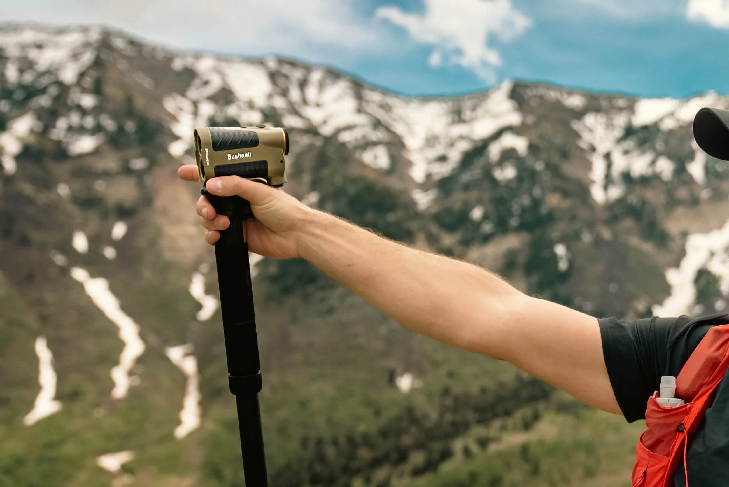 A range finder on a monopod with a hand and arm holding it steady with the Wasatch mountain range behind.