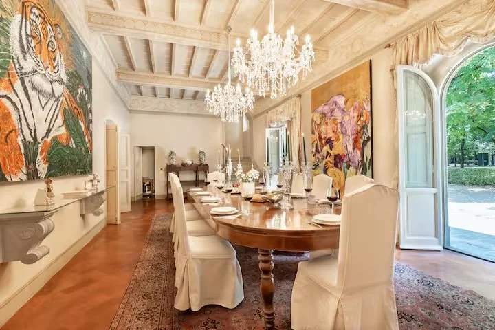 Comedor con una mesa larga, lámparas de araña de cristal y obras de arte.
