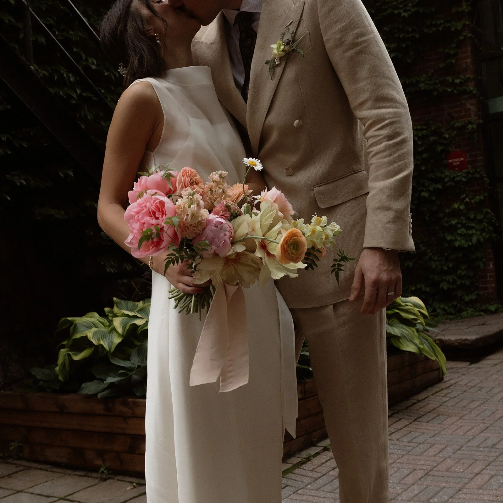 Photo d'un couple de mariés en tenue de mariage, se tenant devant un restaurant à Montréal avec un beau bouquet de fleurs de saison.